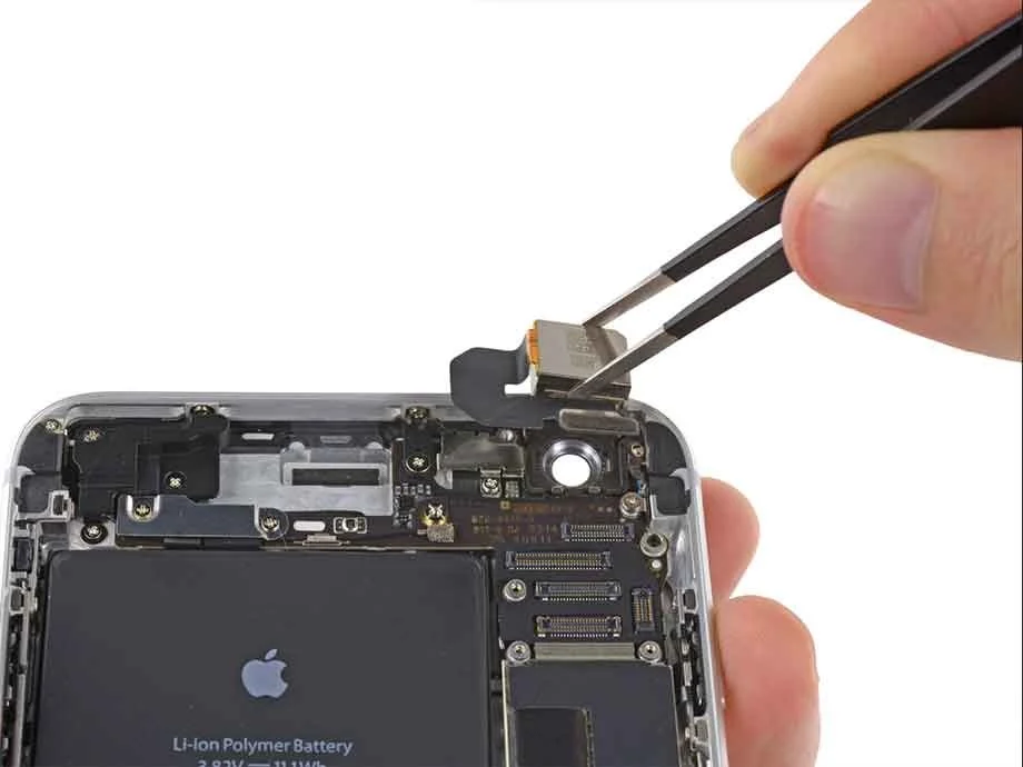 A person using tweezers to handle a small electronic component inside a disassembled iPhone.