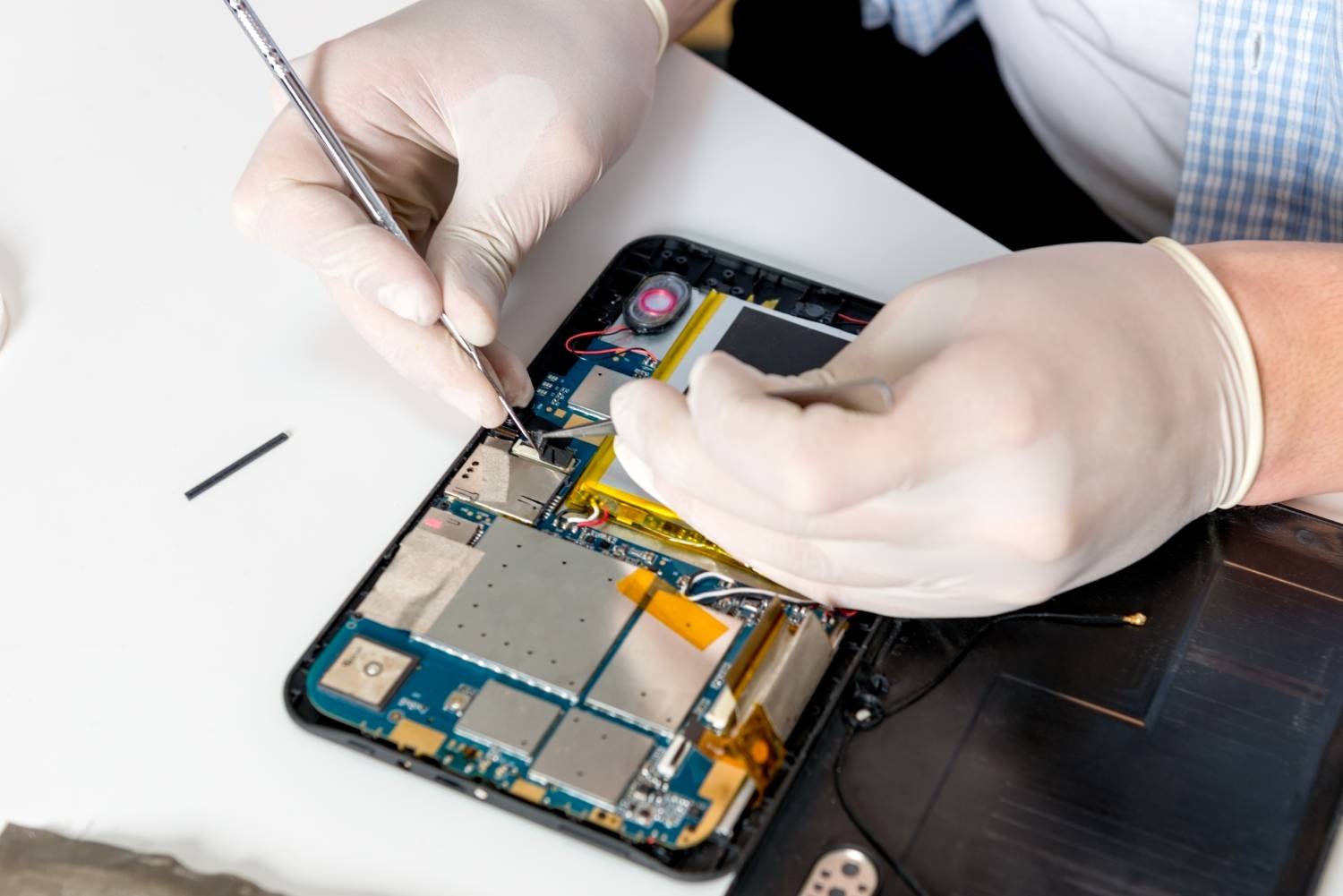 A person wearing white gloves repairing the interior of a disassembled smartphone, working with small tools on the circuit board.