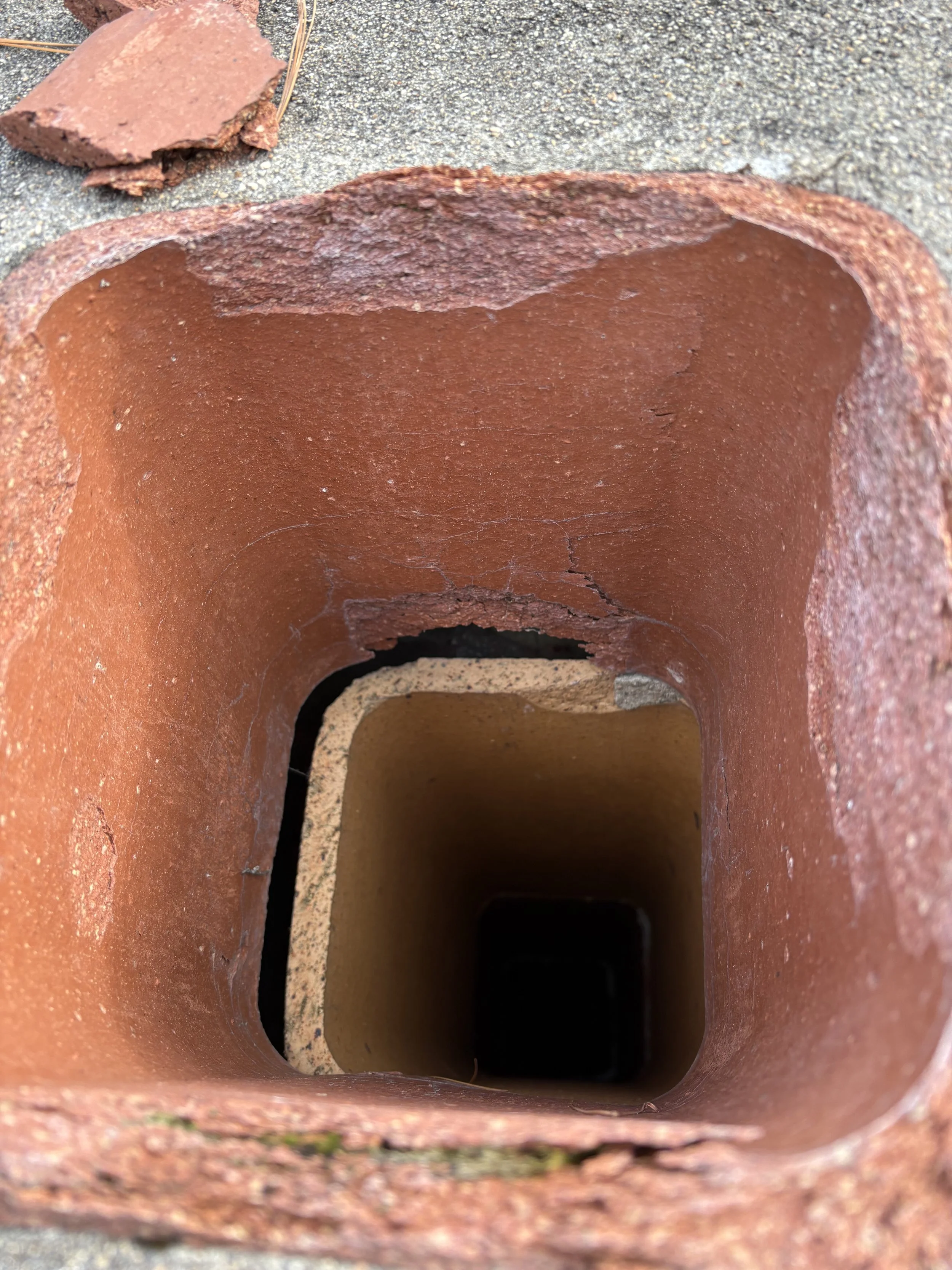 Looking inside an empty, square-shaped brick chimney, with visible cracks and rough texture. Needs a liner installed by Silas Miller Stove & Chimney
