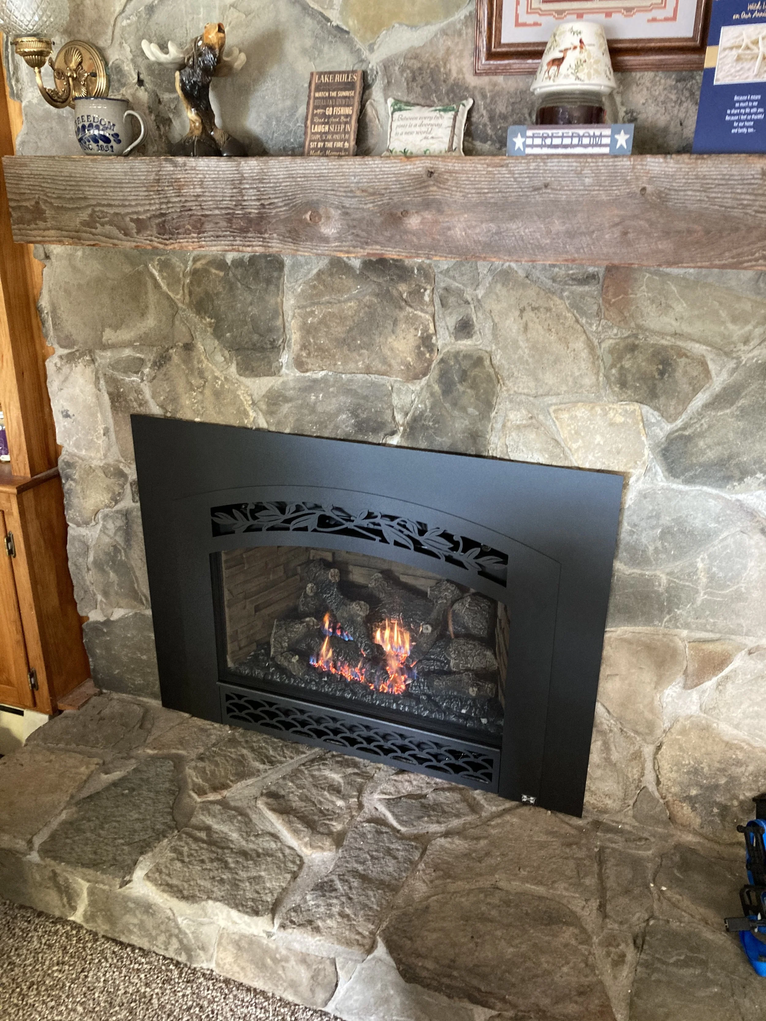 Stone fireplace with a black gas insert and a fire burning inside. beautiful stone veneer and installation just completed by Silas Miller Stove & Chimney