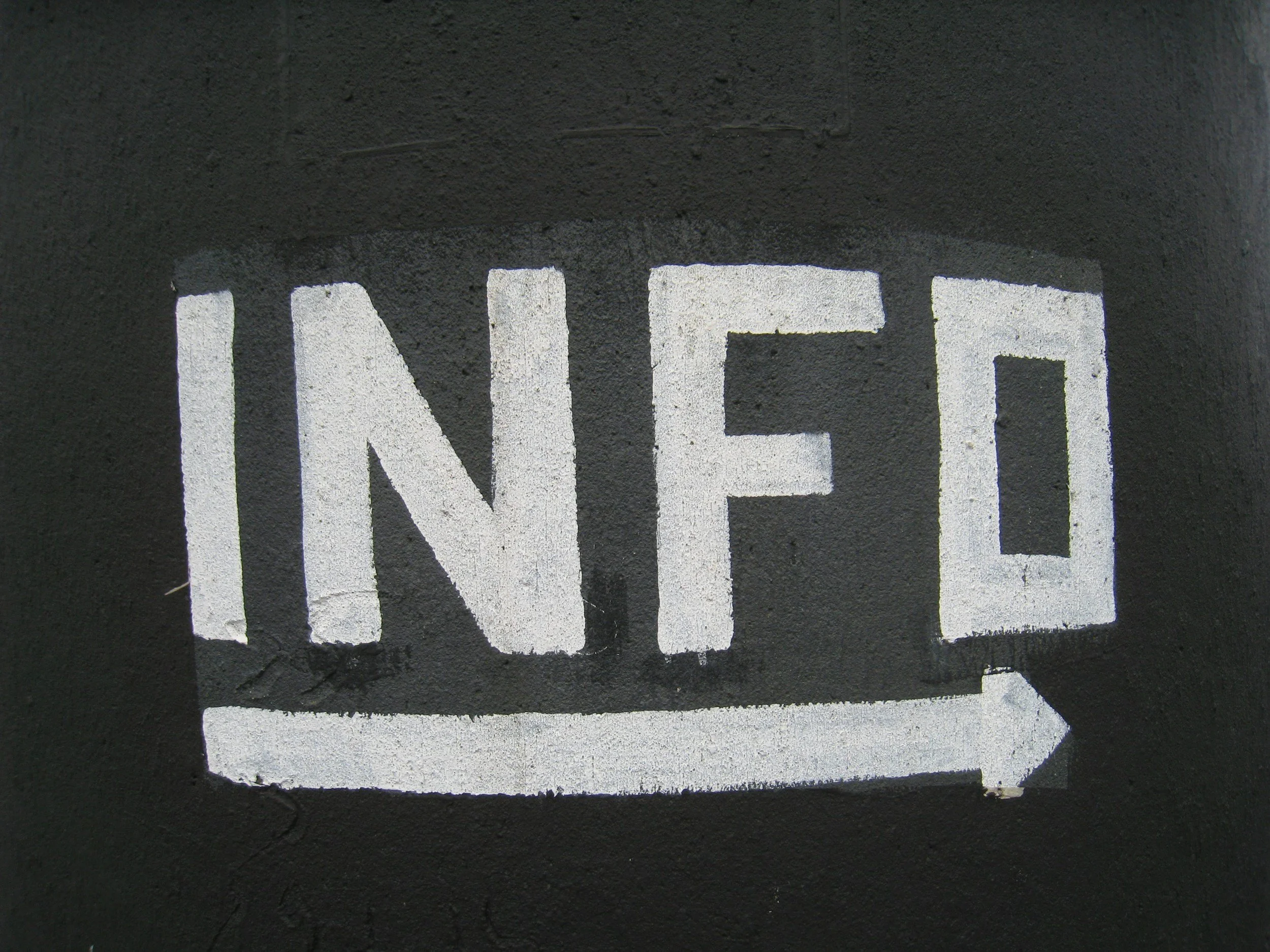 White painted 'INFO' sign with an arrow pointing to the right on a black background.