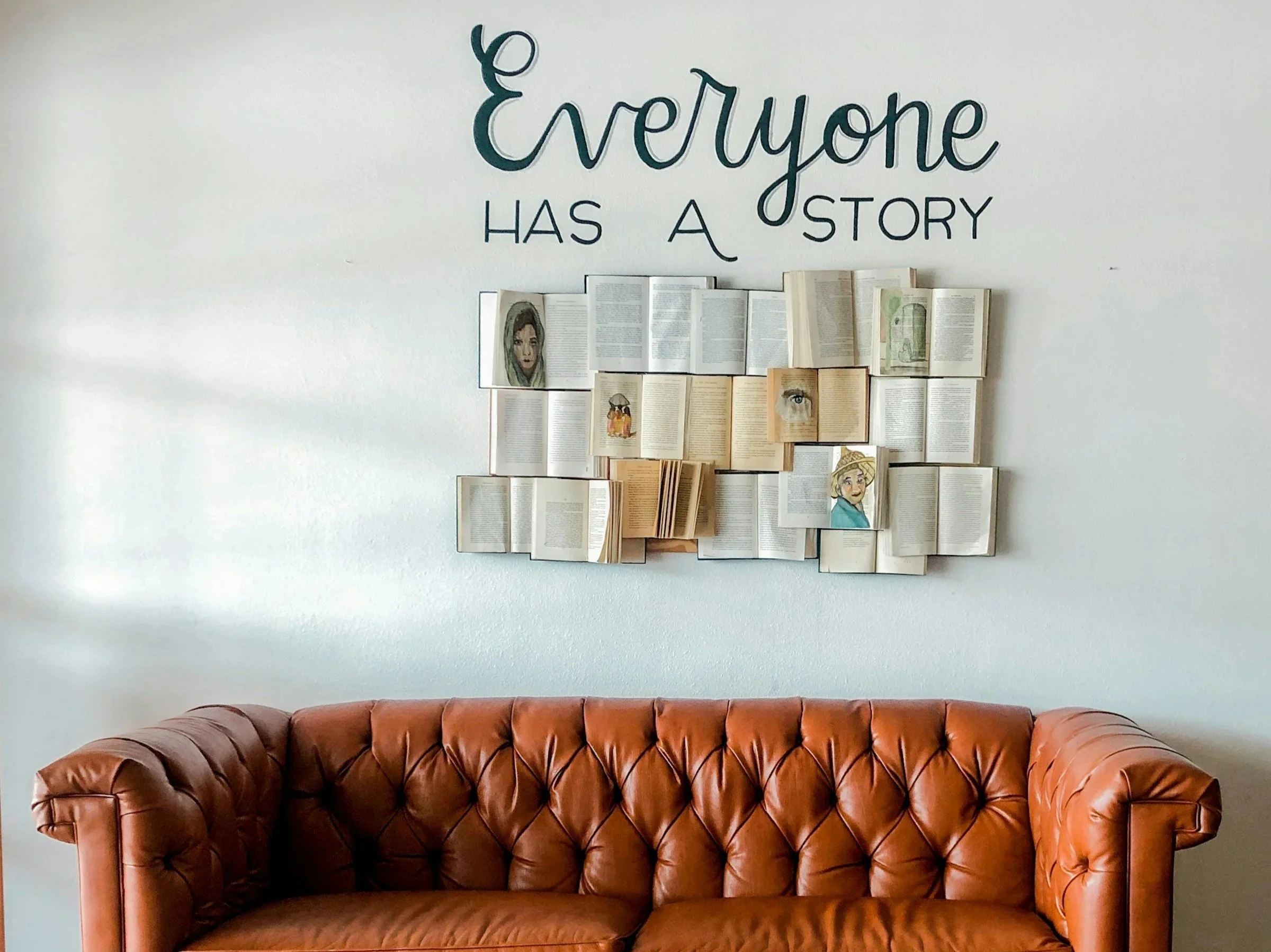 Decorative wall art with books and portraits above a brown leather tufted sofa