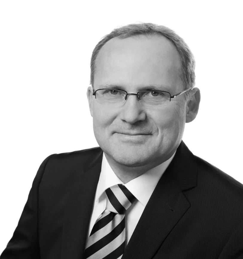Schwarz-weiß Portrait eines Mannes in Anzug und Krawatte, trägt Brille, vor weißem Hintergrund.
