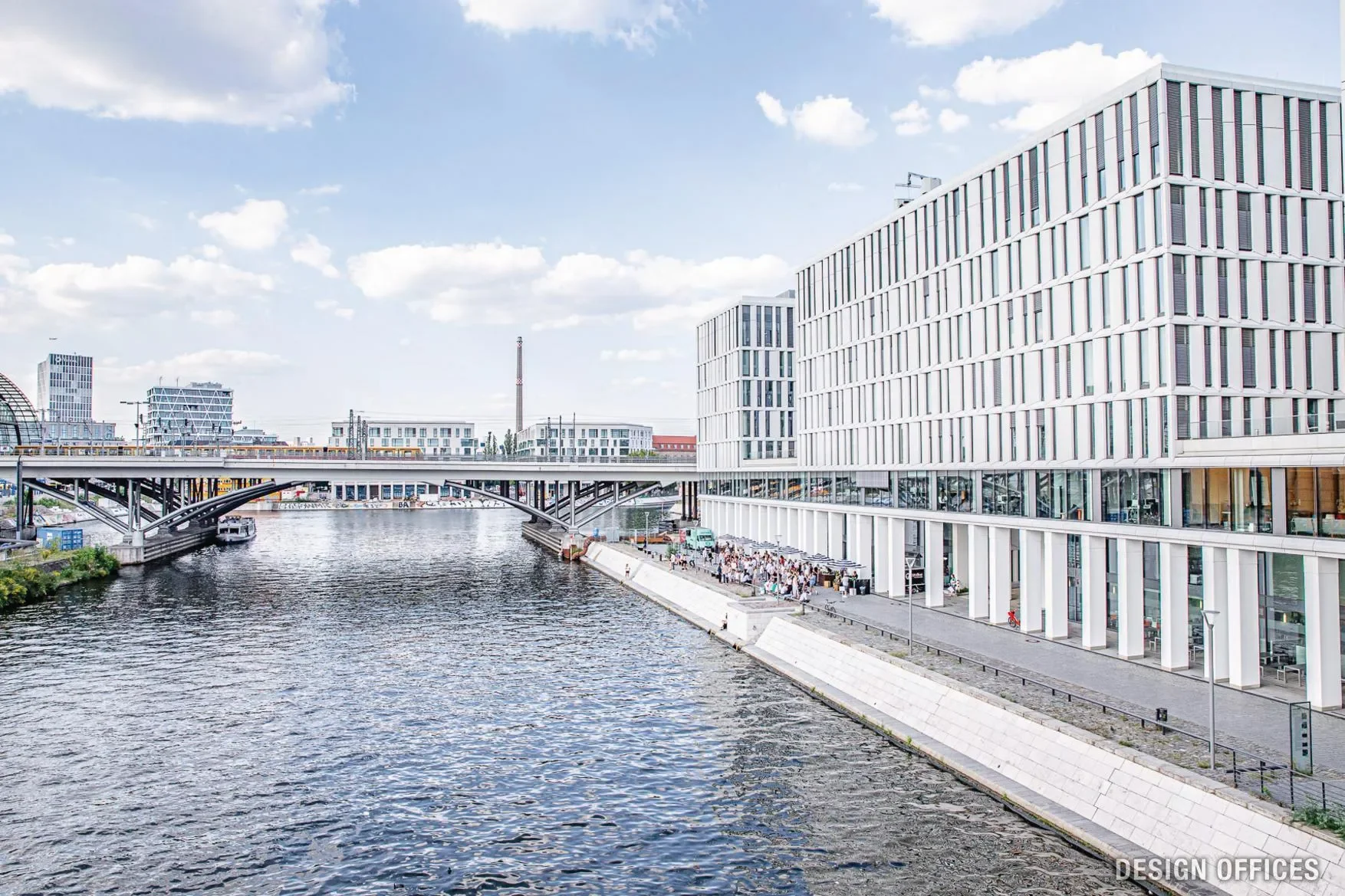 Moderne Bürogebäude neben einem Fluss in einer Stadt bei sonnigem Himmel.