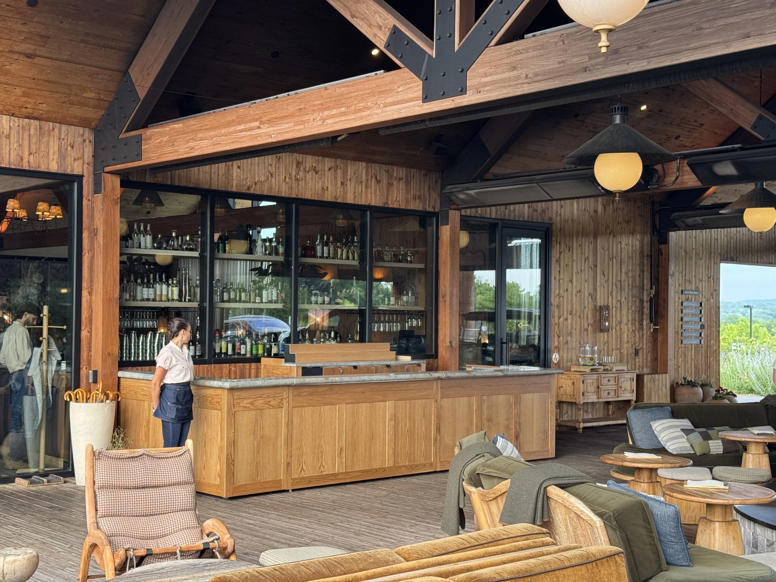 Interior of a rustic restaurant with wood paneling, a bar with bottles, and various seating areas with chairs and couches.