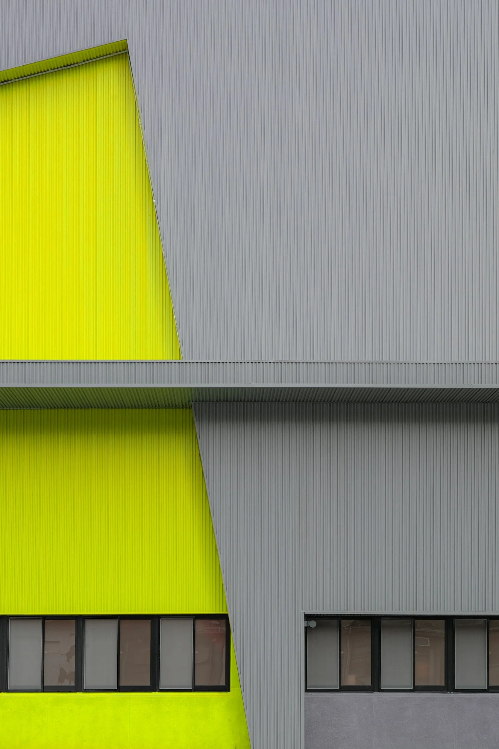 Close-up of a modern building with vibrant yellow and gray corrugated metal panels and black-framed windows.