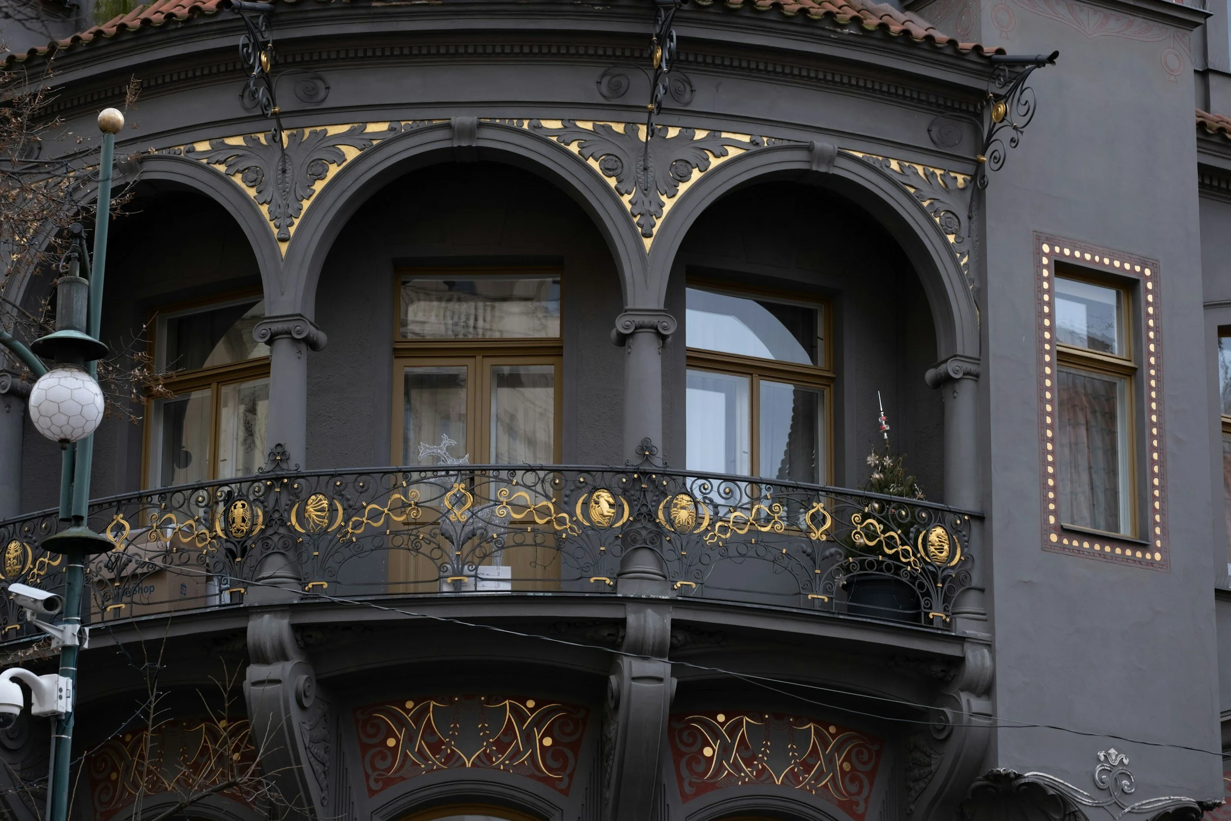 The facade of an ornate, dark gray building with curved windows, decorative gold accents, and a small Christmas tree on the balcony.