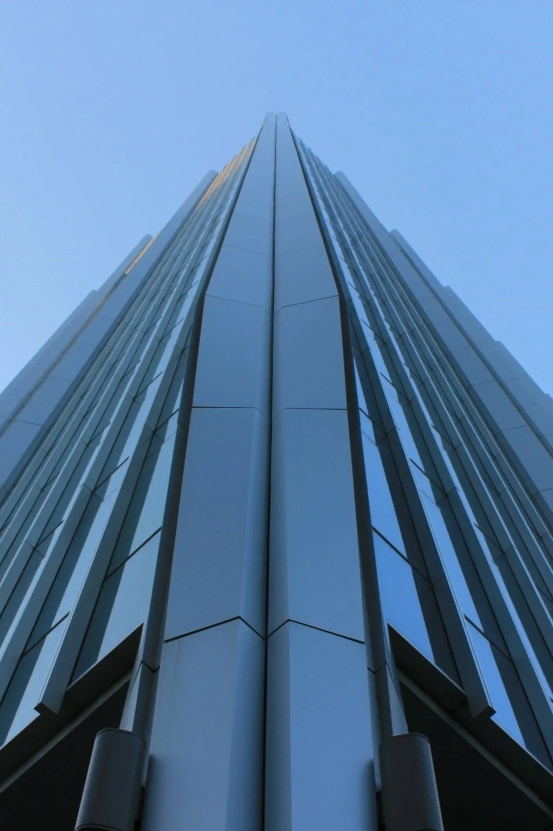 Low angle view of a glass skyscraper against a clear blue sky.