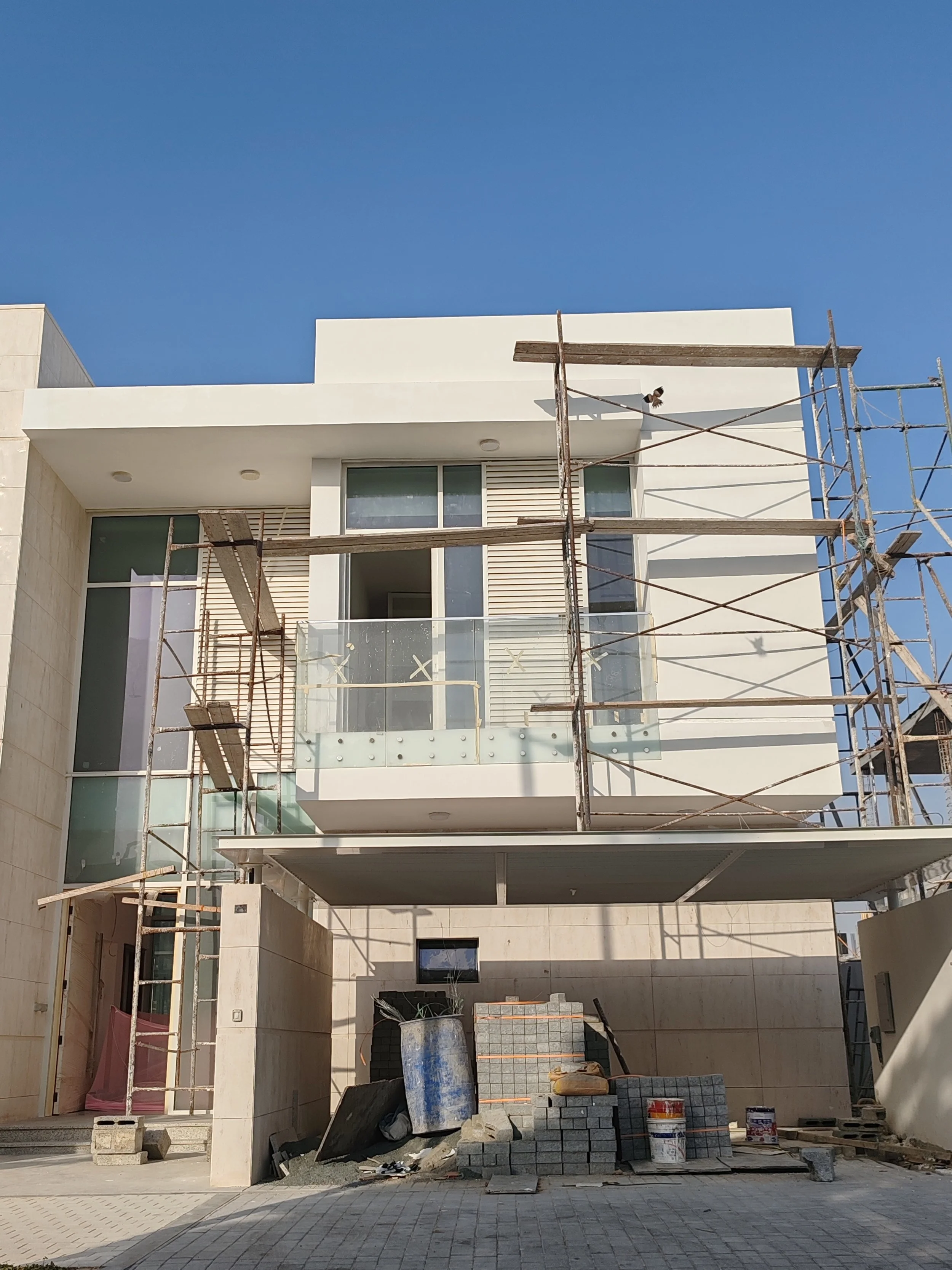 Modern white multi-story house under construction with scaffolding and building materials in front.