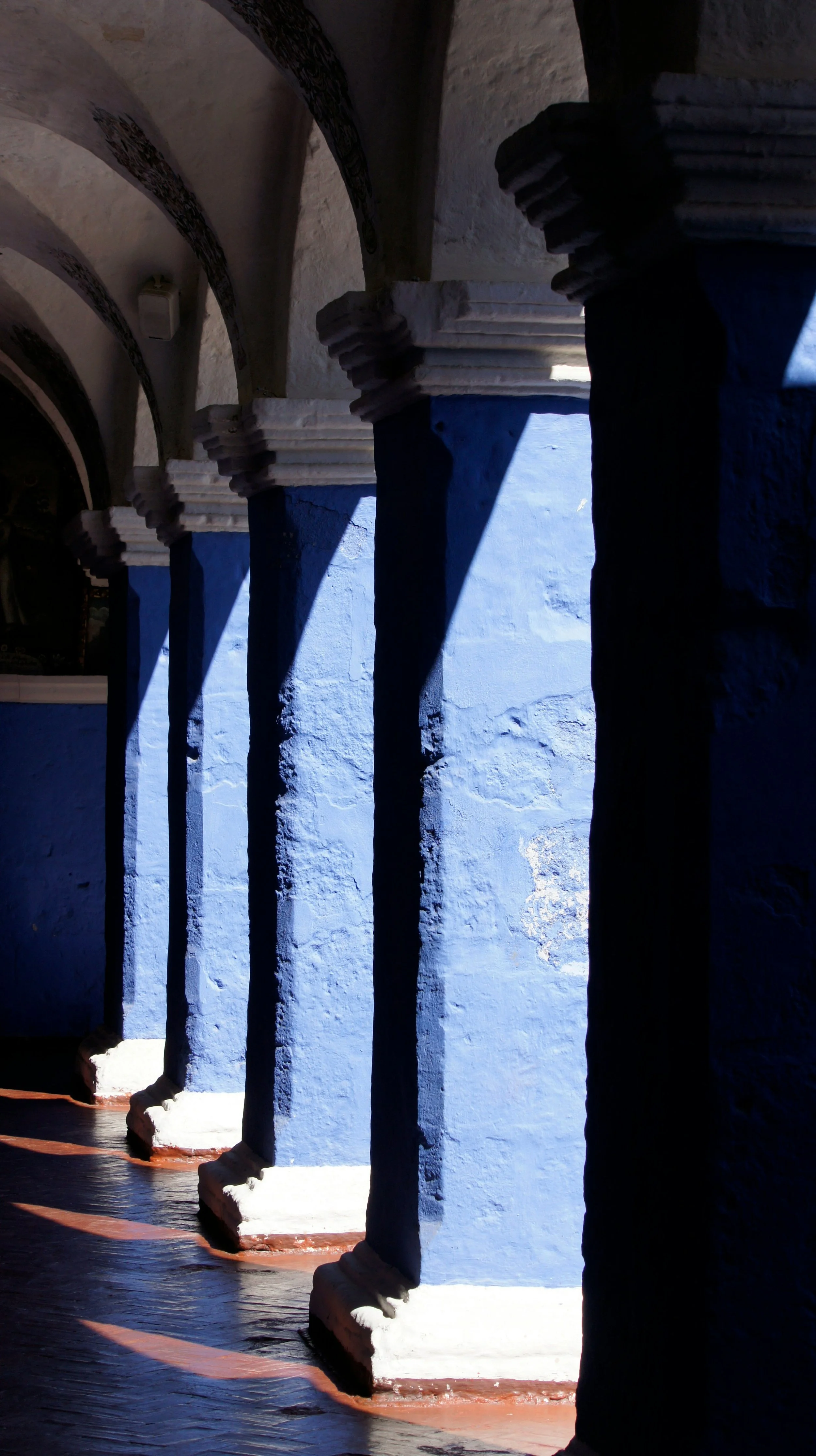 Blue columns with white bases in a corridor with arched ceilings, sunlight casting shadows.