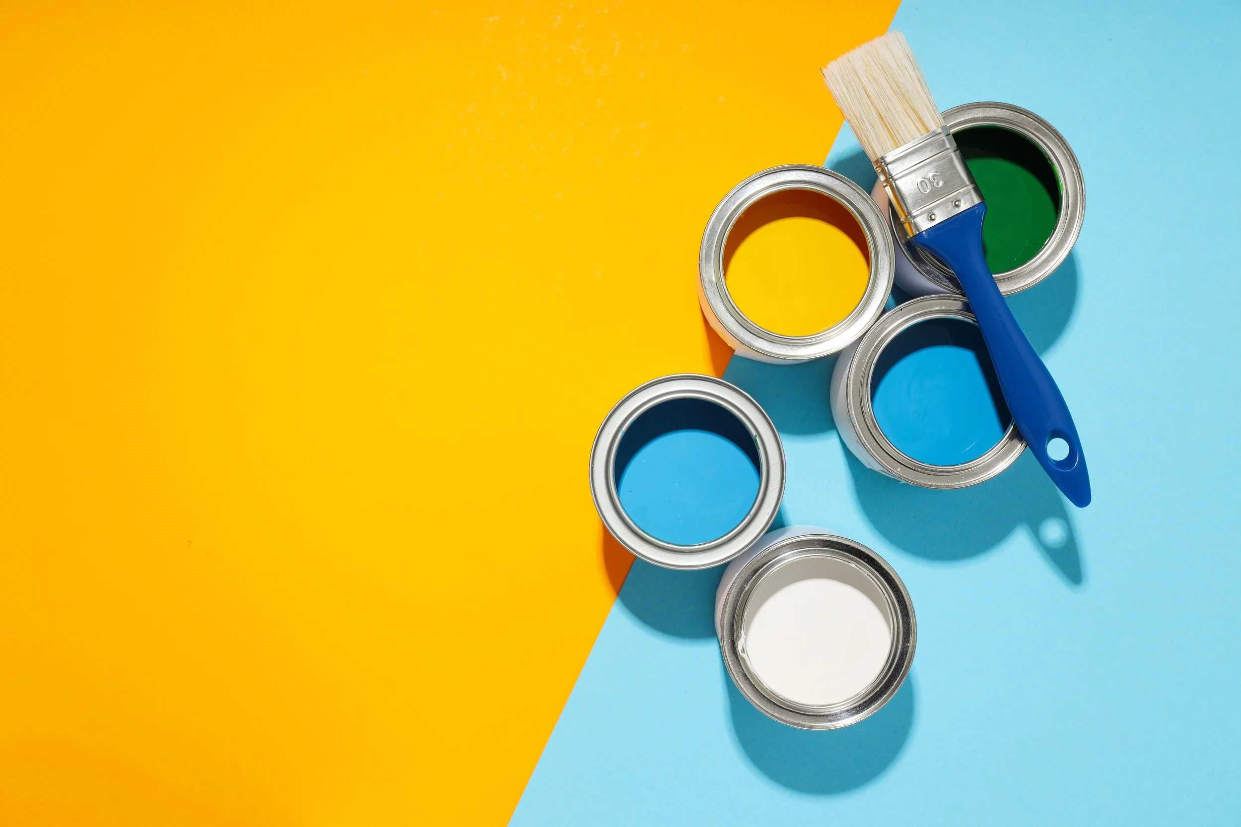 Open paint cans with yellow, green, blue, and white paint, along with a paintbrush with blue handle, on a yellow and blue background.
