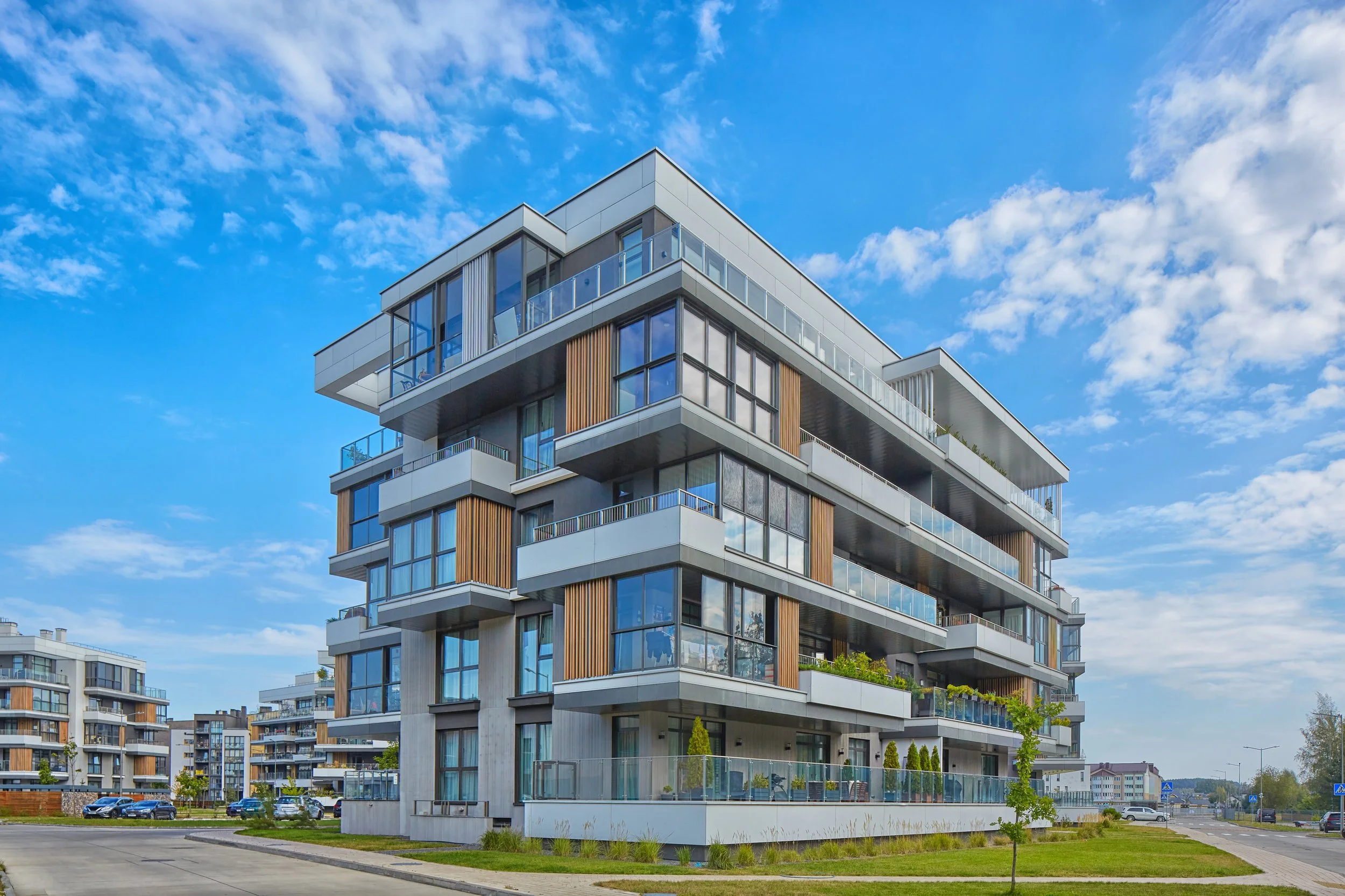 Modern multi-story apartment building with glass balconies, located in a suburban area under a partly cloudy sky.
