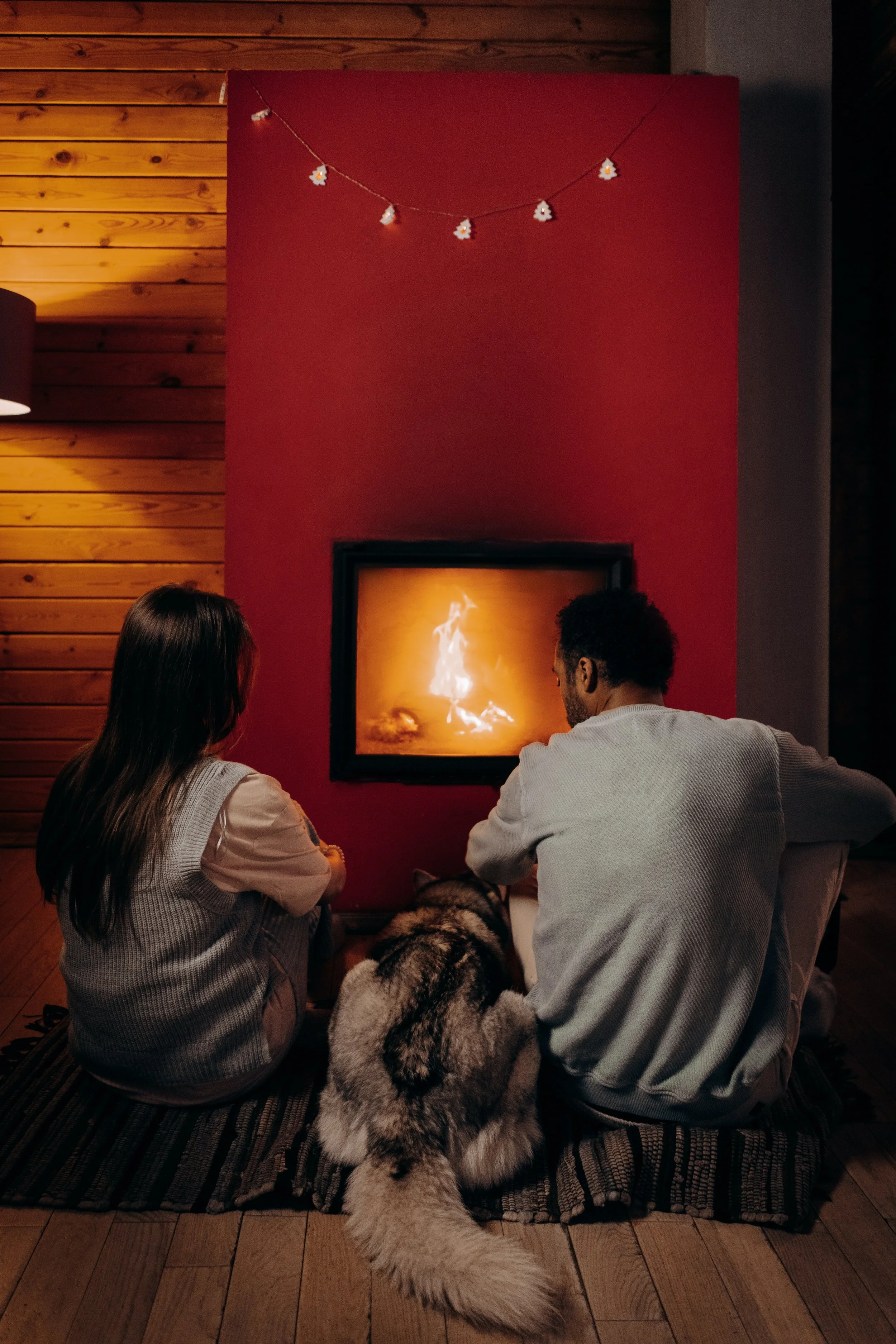 Red wall with cosy open log fire and two people sitting in front