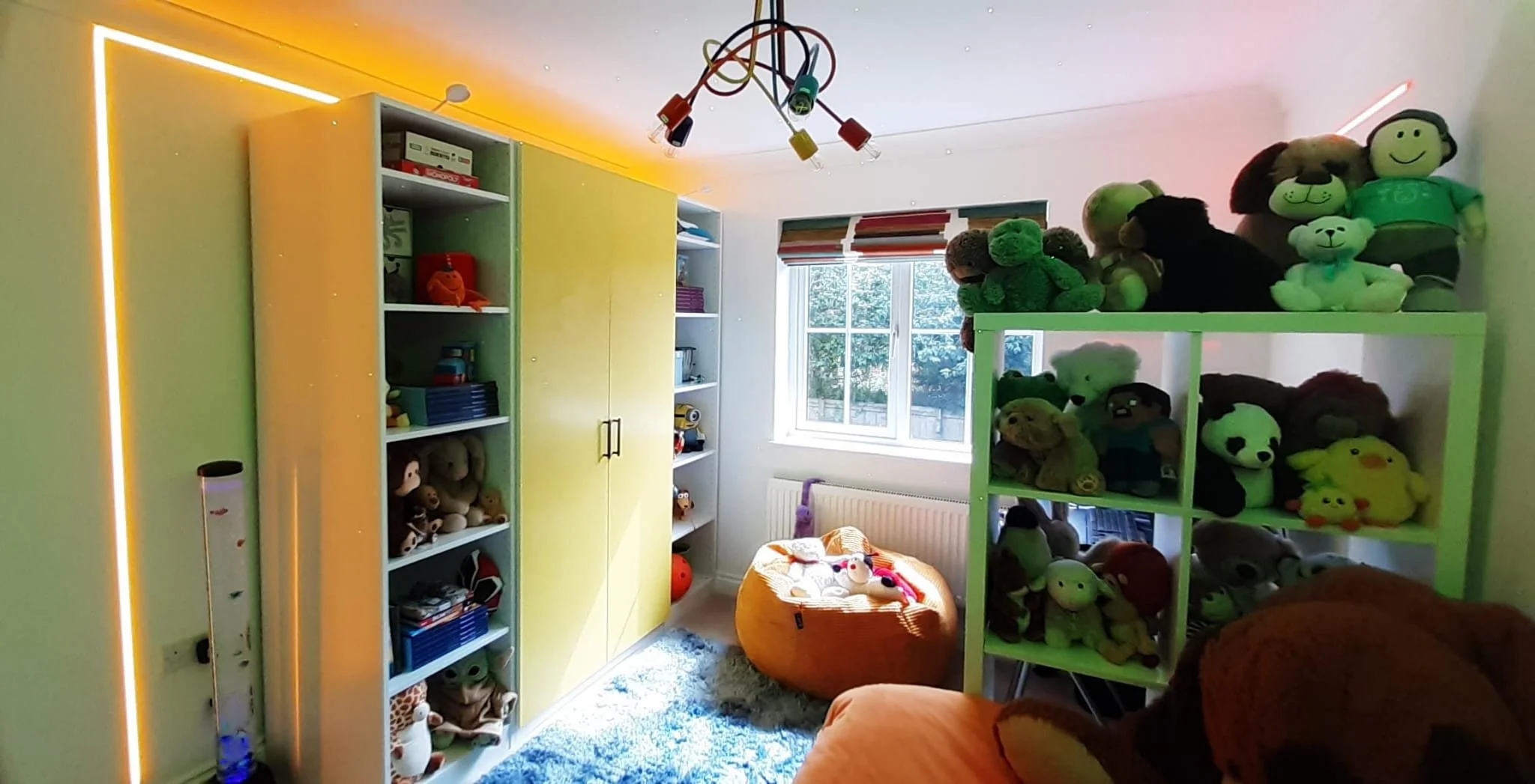 Fitted yellow storage units with yellow LED lighting in gaming bedroom redesign, Northamptonshire, featuring open shelving and closed cupboard storage alongside tall illuminated acrylic bubble floor lamp