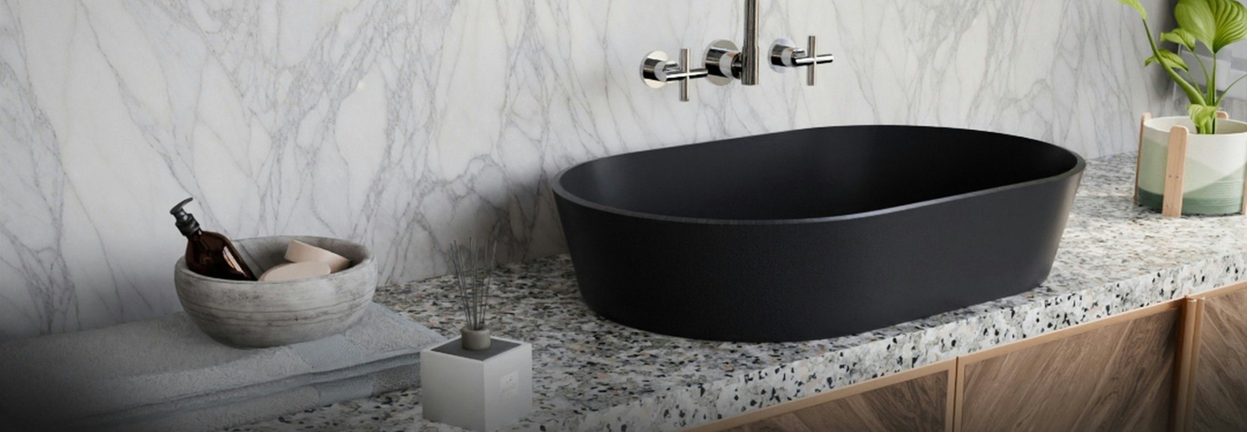 A sculptural cloakroom basin in dark grey porcelain with marble backsplash and a terrazzo worktop