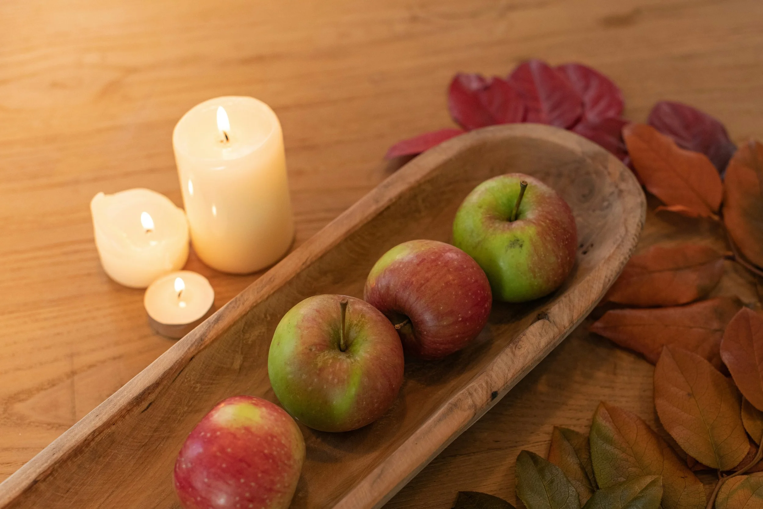 red apples in a wood trug with autumn leaves and candles