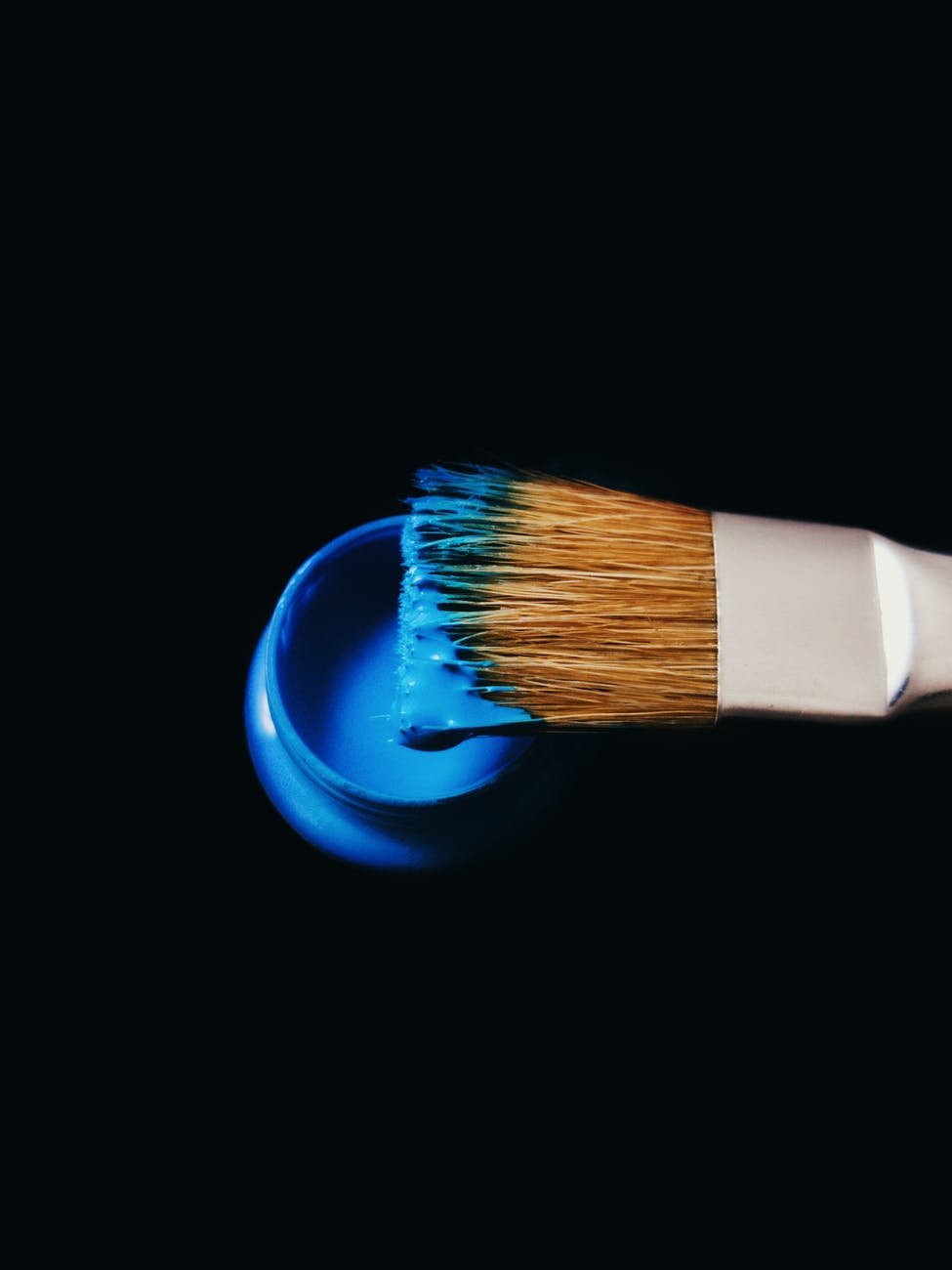 Paintbrush and sample pot of bright blue paint against a black background