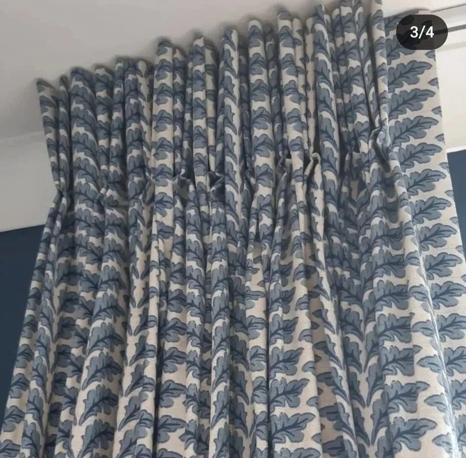 A set of bespoke blue and white patterned curtains with a leafy design hanging on a window.