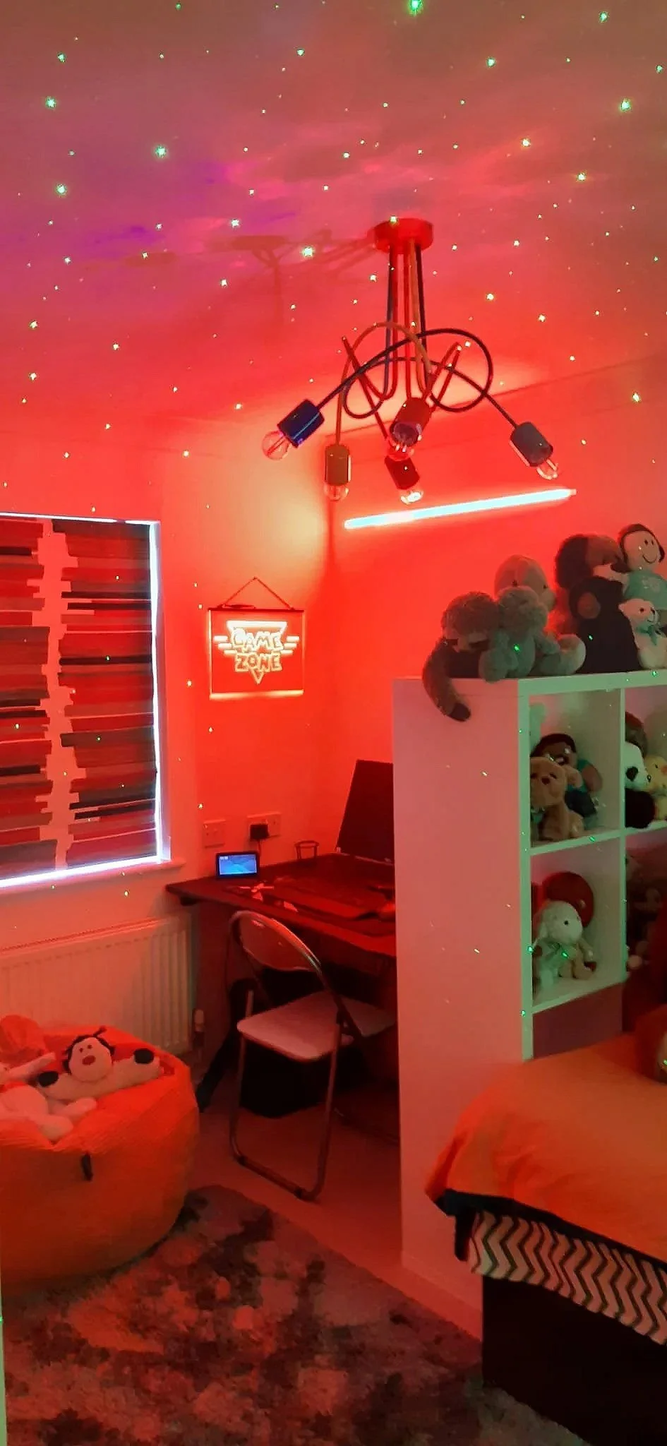 Gaming bedroom redesign in Northamptonshire with red LED atmosphere lighting, illuminated Game Zone neon sign, galaxy ceiling projector and white cube storage unit displaying soft toy collection