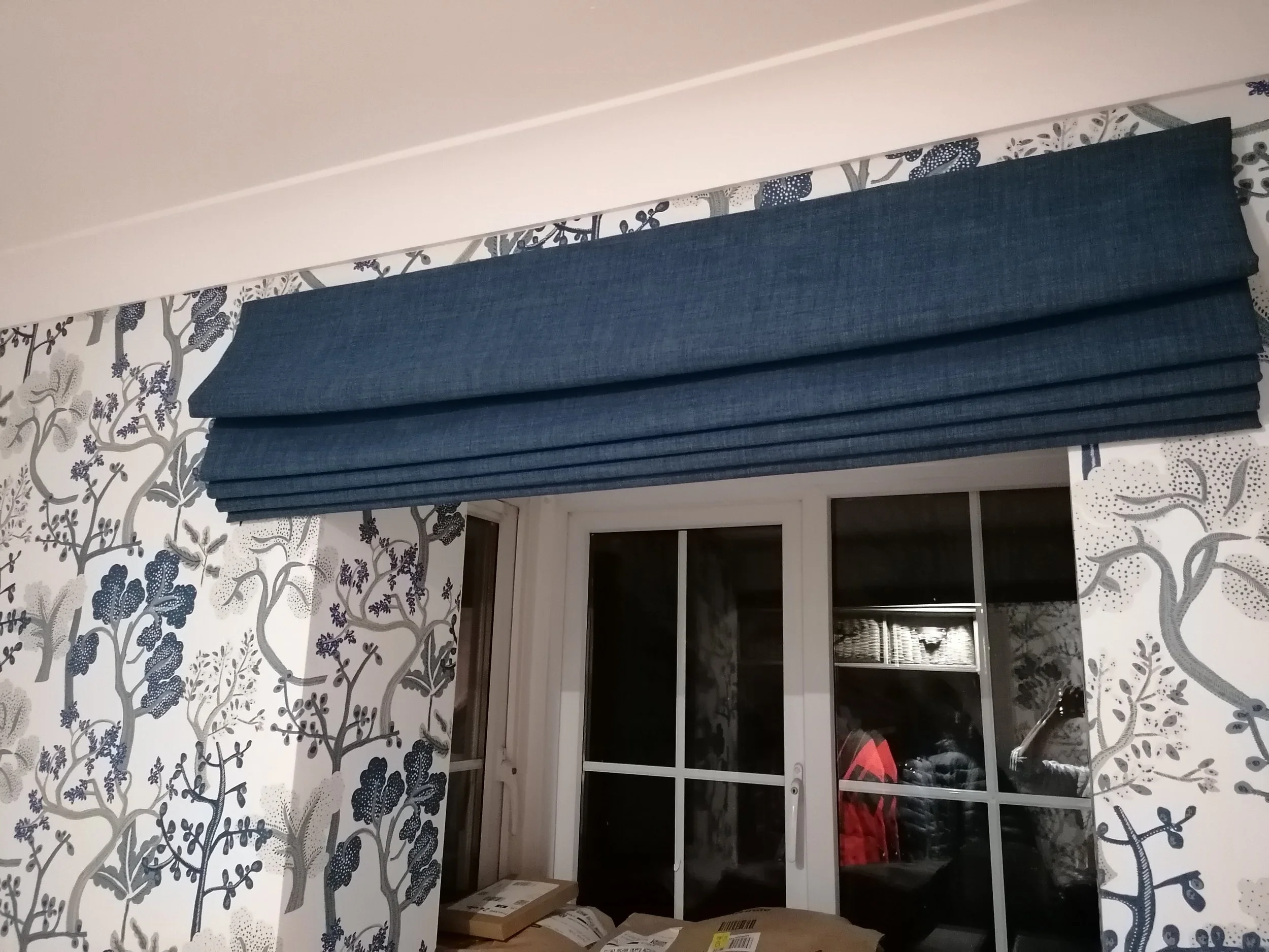 Interior view of boot room with patterned wallpaper, a window with a bespoke Roman blind.