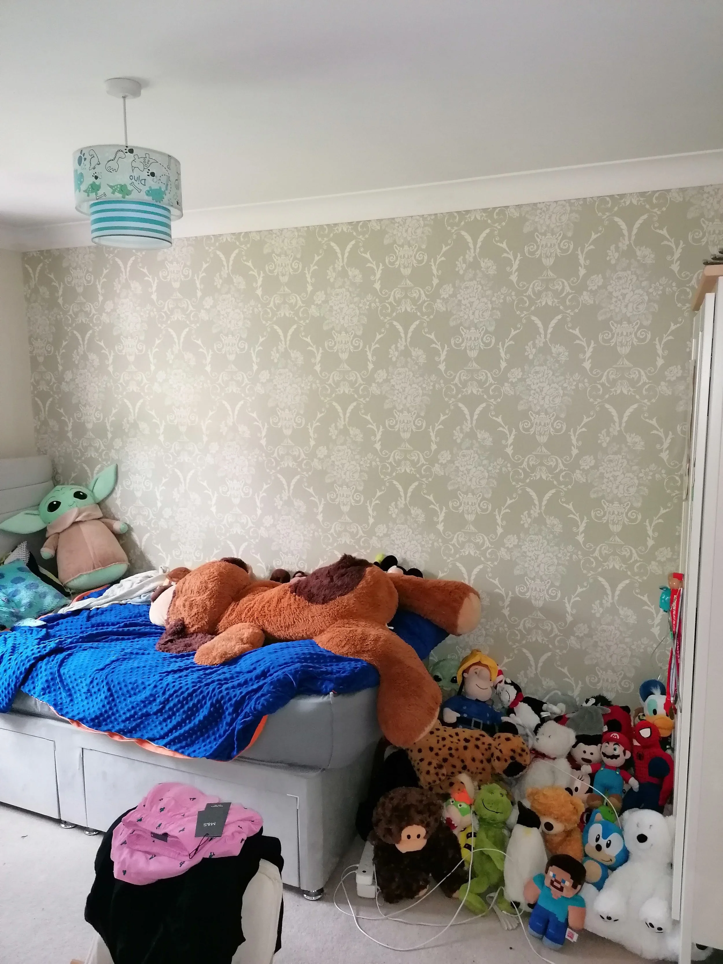 Before: Child's bedroom in Northamptonshire with sage green damask feature wallpaper, grey upholstered bed and large soft toy collection prior to redesign by Omorfia Interior Design