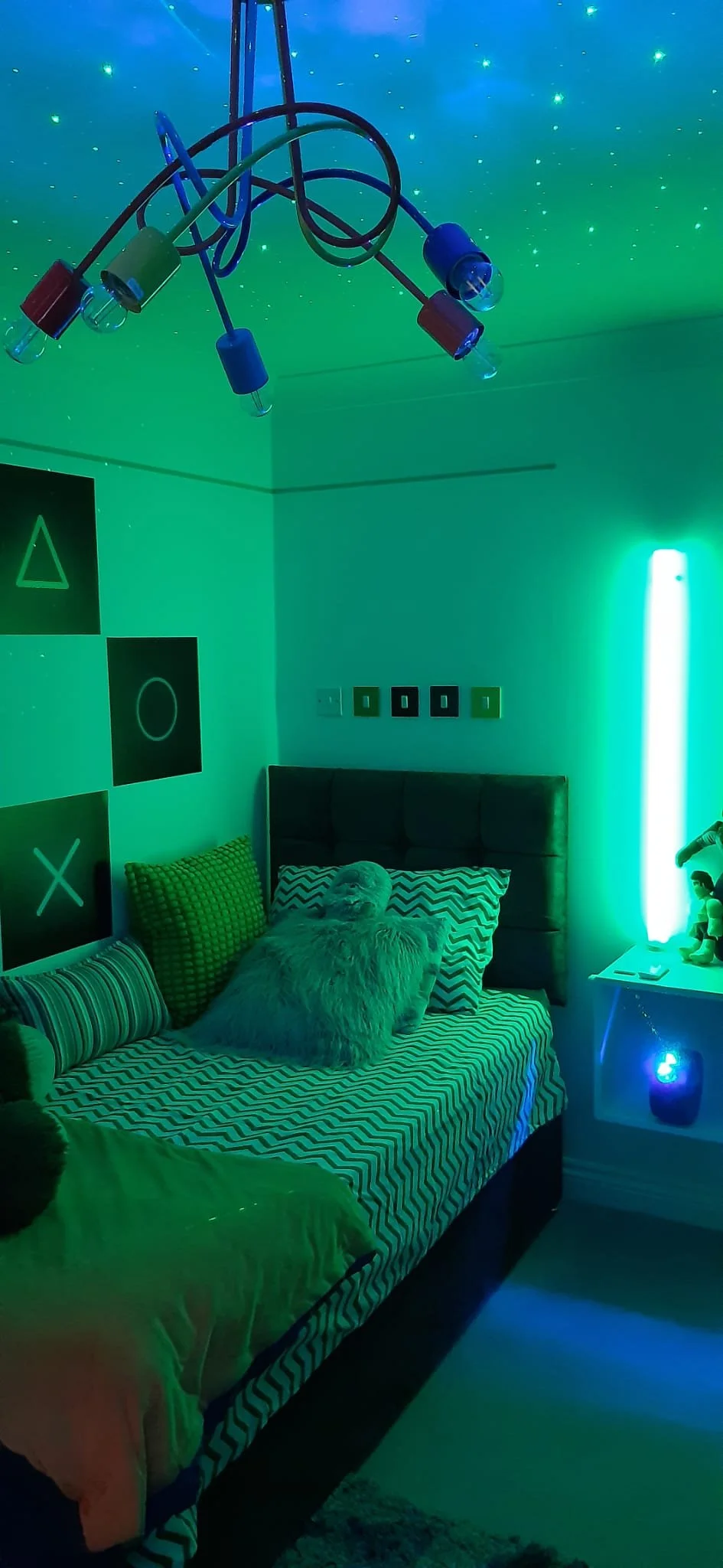 Gaming bedroom redesign in Northamptonshire bathed in green LED strip lighting with galaxy ceiling projector and bubble lamp by bed