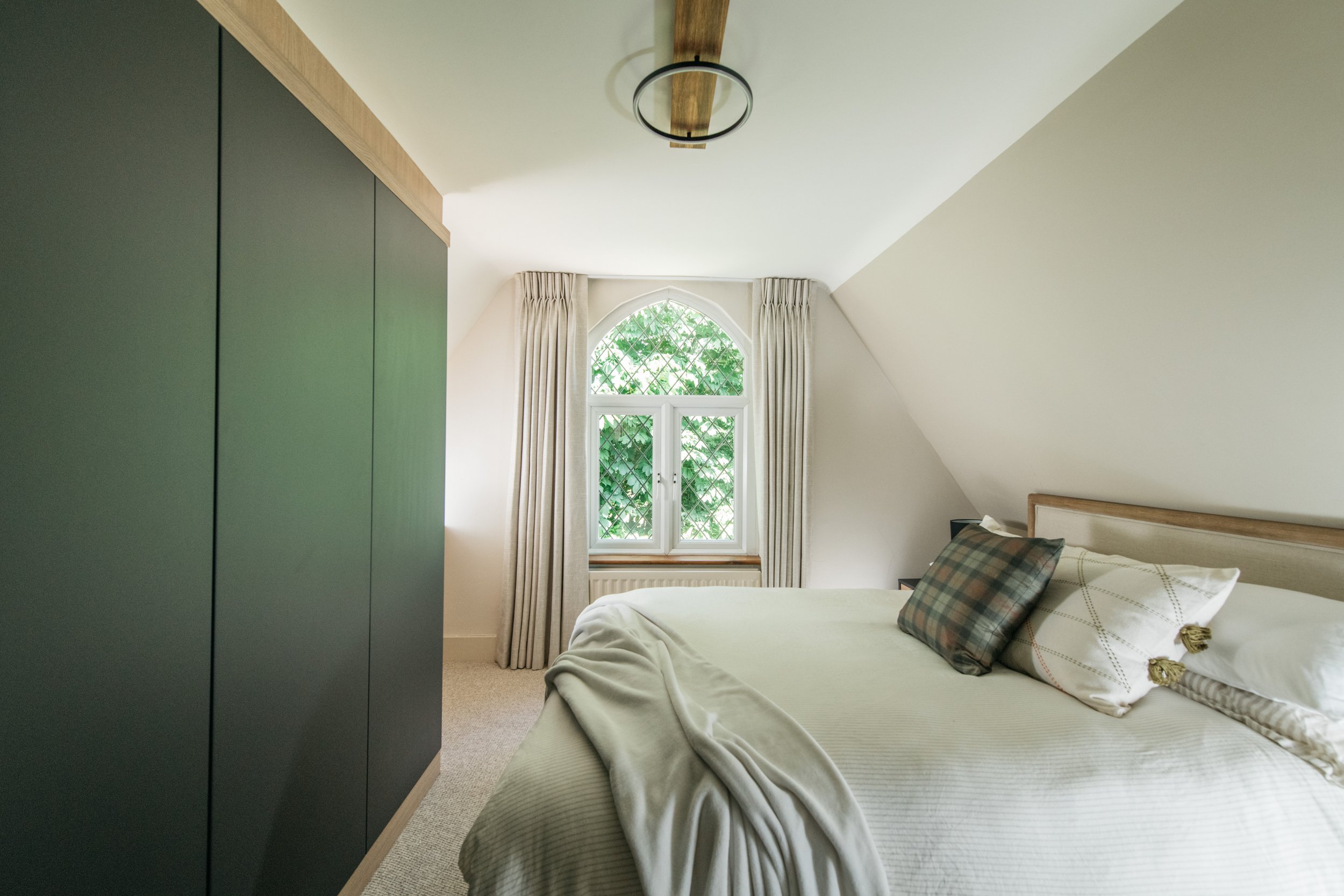 A bedroom with a bed, pillows, a window with curtains, and a ceiling light fixture.