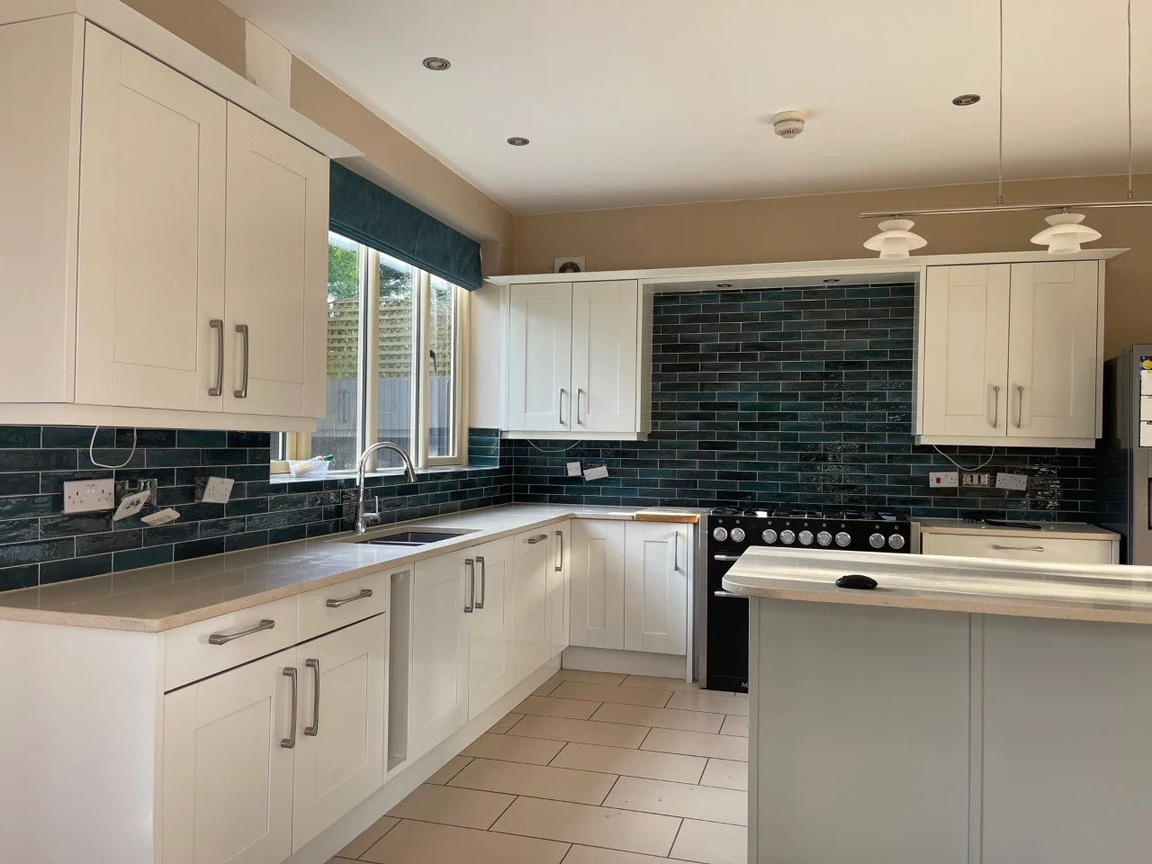 Kitchen with white cabinets, beige countertops, dark green backsplash tiles, a window with a view outside, and a stove.