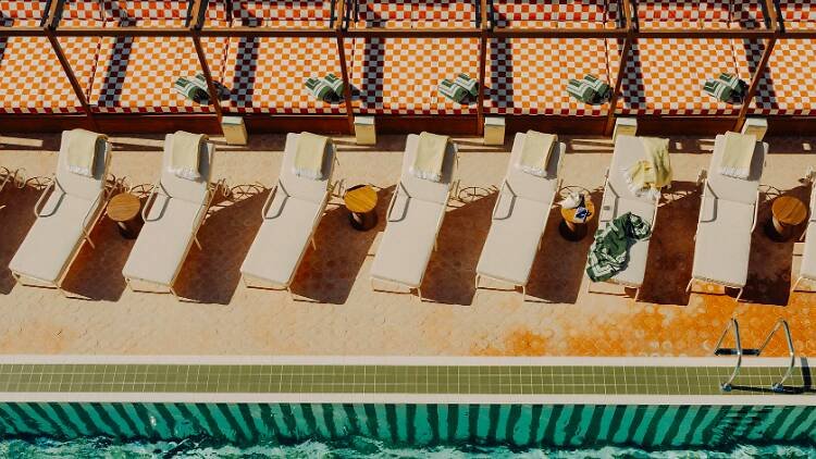 Sillas de tumbona junto a una piscina, algunas con toallas y objetos personales.