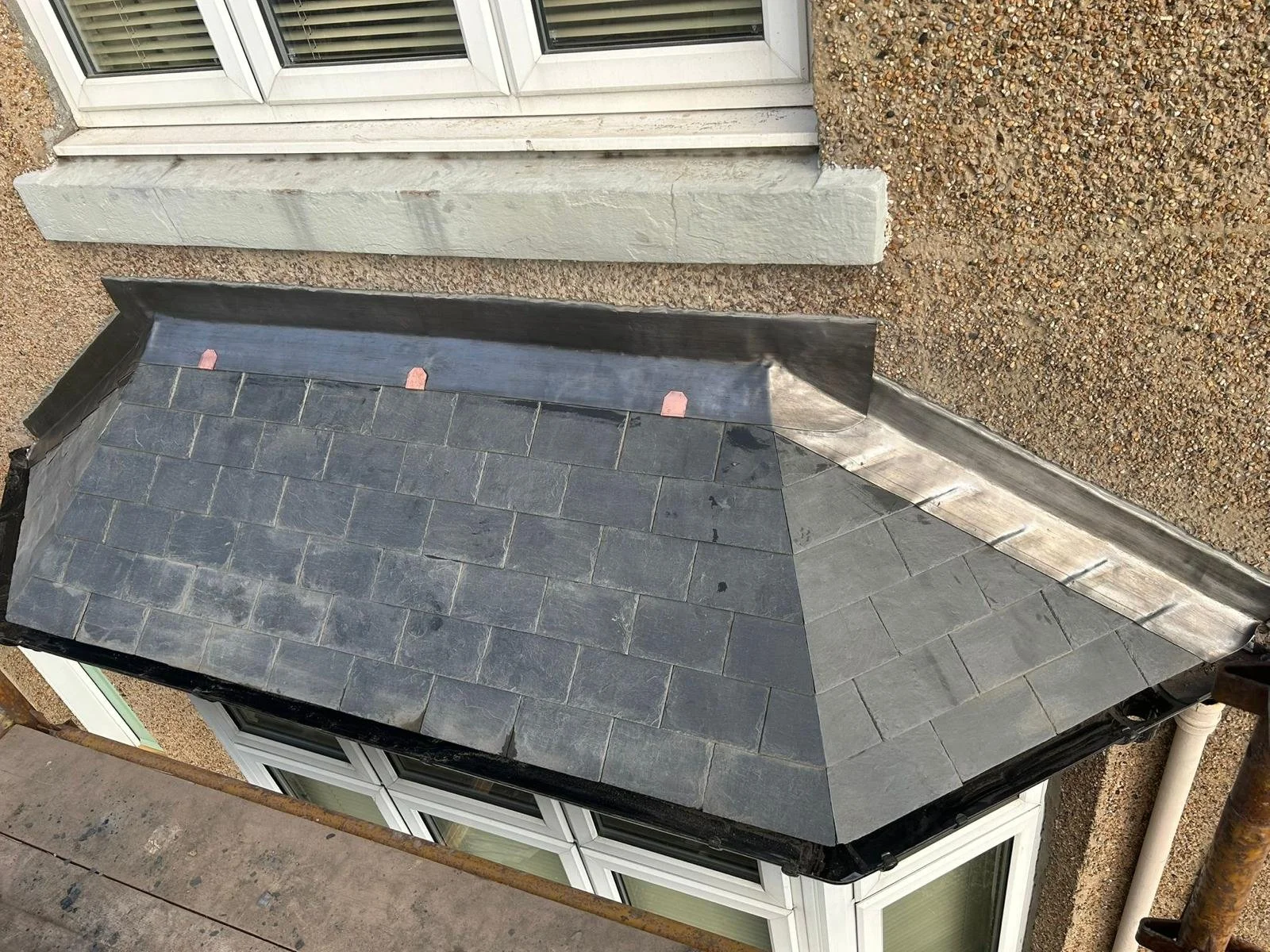 View of a sloped roof with dark gray slate tiles, adjacent to a window and a textured brick wall, showing construction or renovation work. Re slate of roof in scottish borders