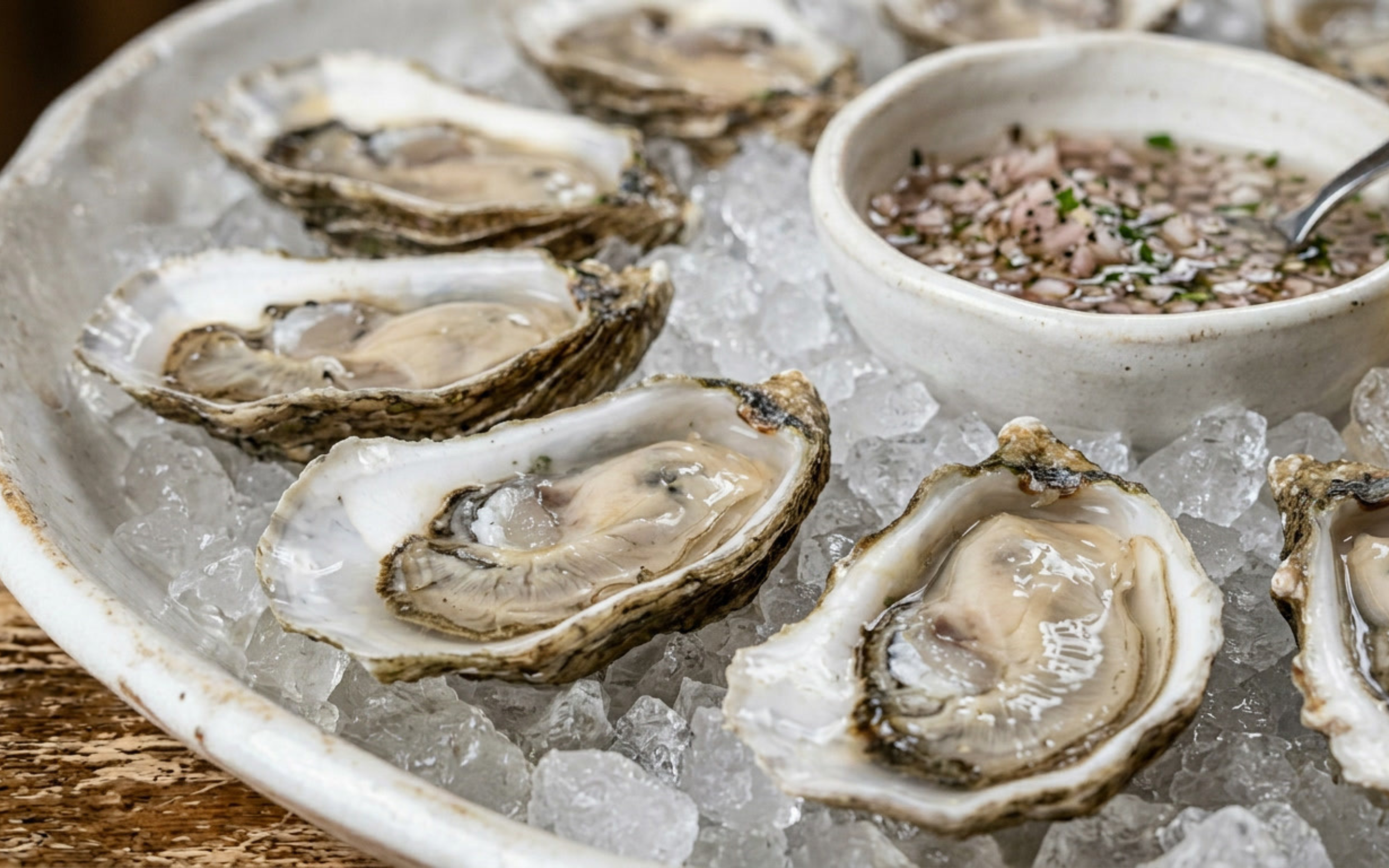 Fresh oysters served on ice with a bowl of chopped shallots and vinegar cocktail sauce.