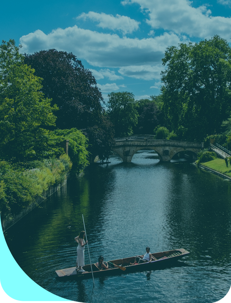 Photo of a river in Cambridge with a bridge in the background and people punting in the foreground