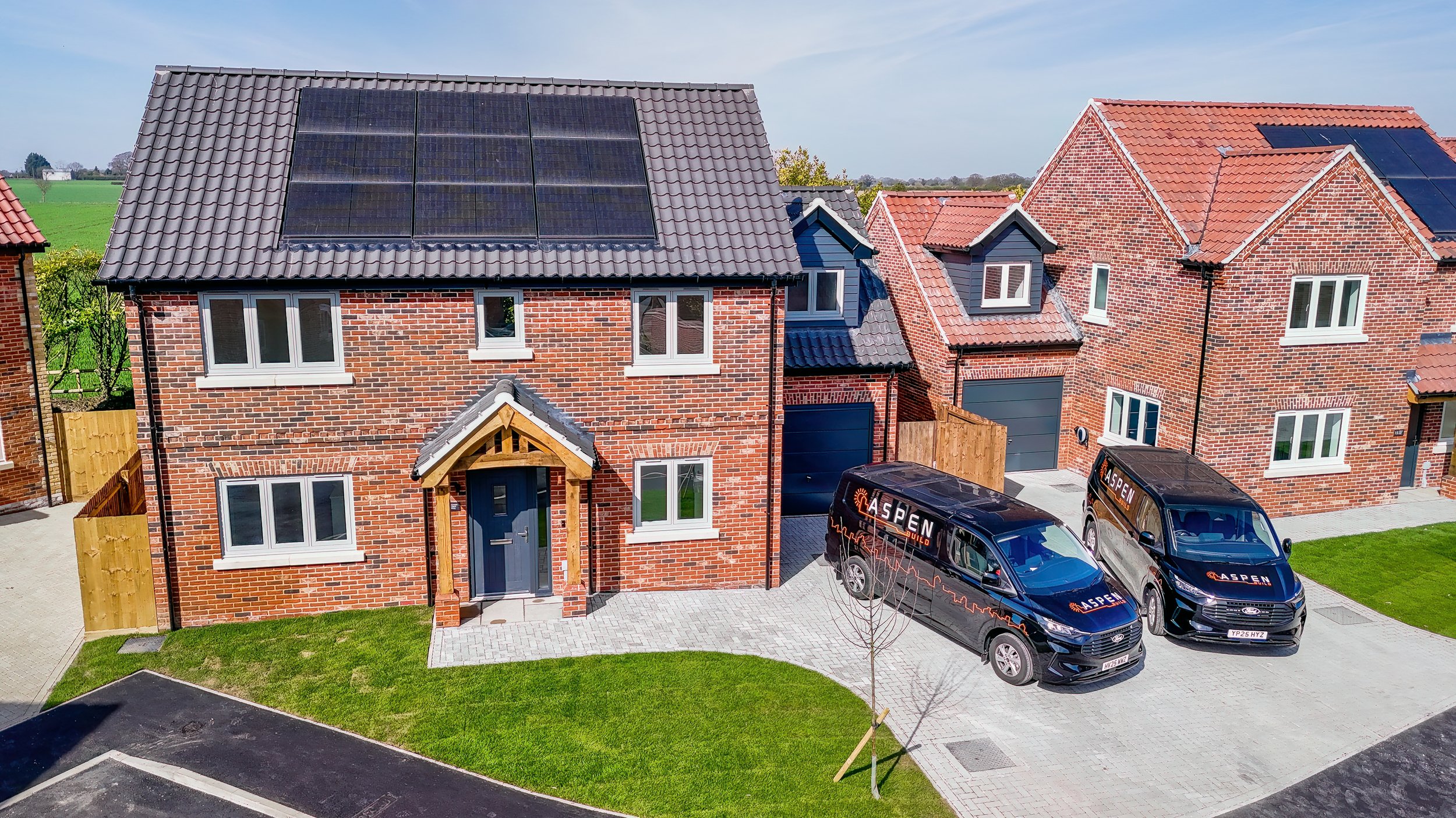 Red-brick homes with solar panels and Aspen Build vans at The Green