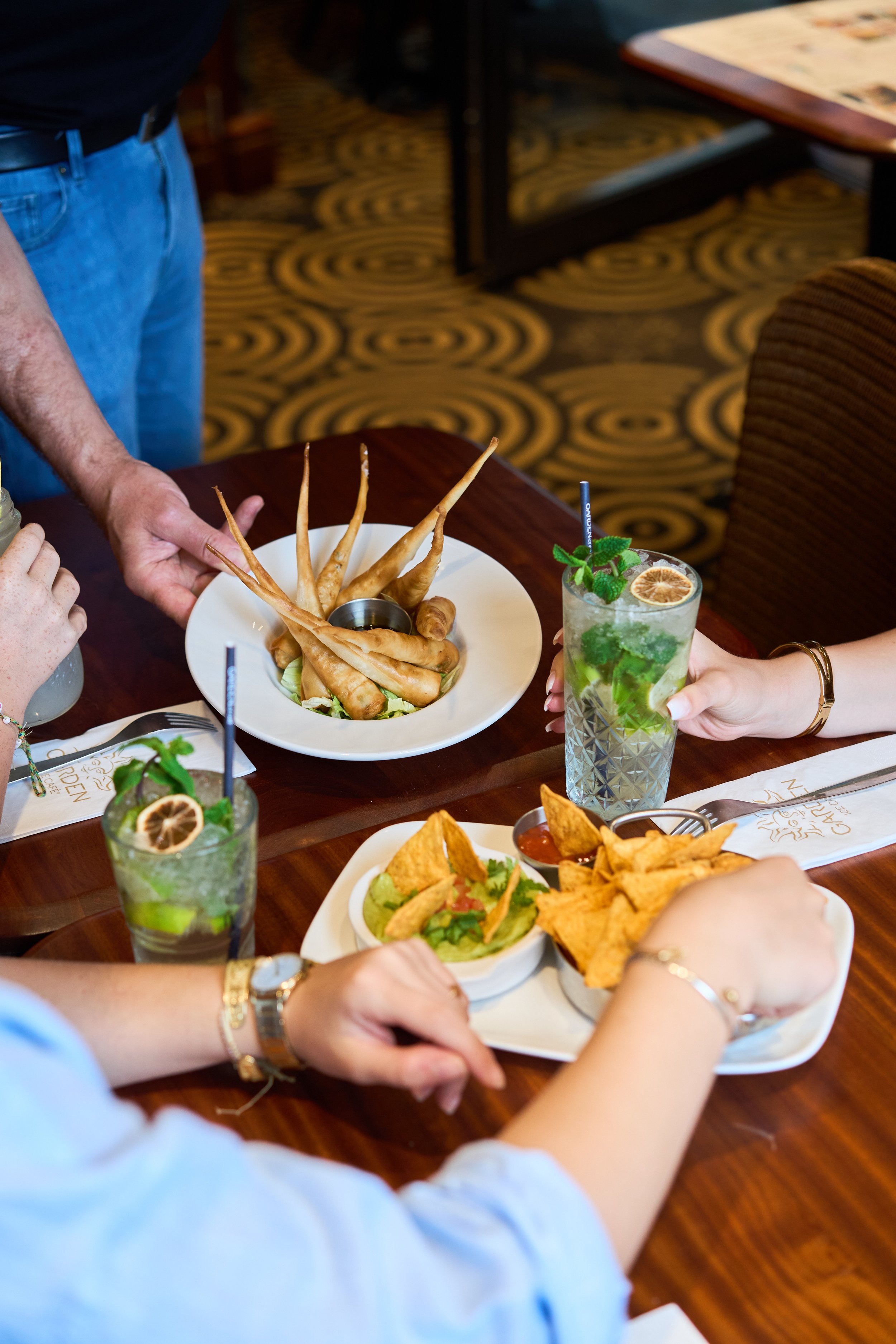 Assiette de nourriture variée comprenant des tranches de jambon, des olives, du houmous avec des morceaux de légumes, des rondelles d'oignons frits, du guacamole, du pain pita coupé en triangles, des chips, des sauces, au garden Ice
