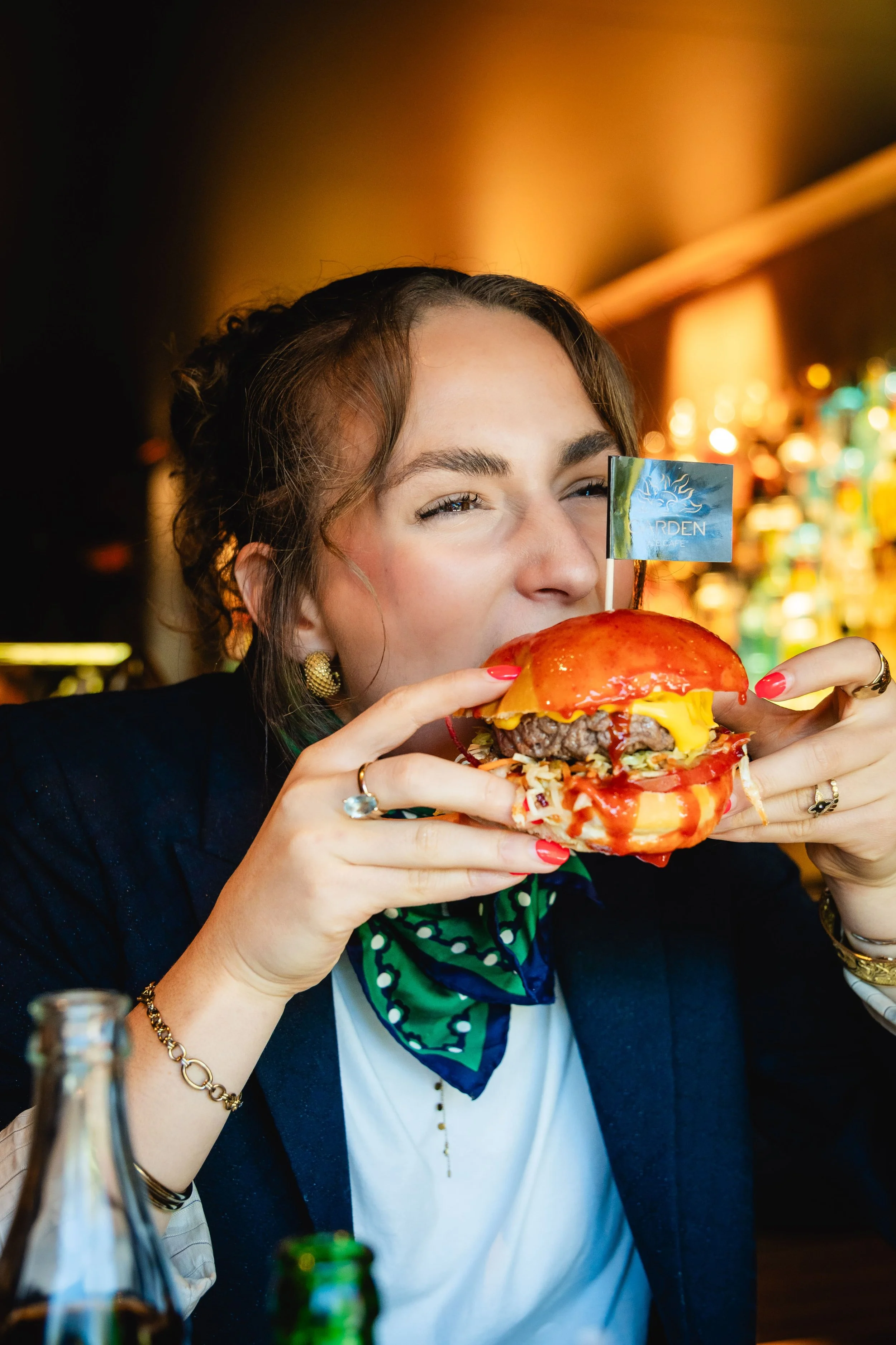 Une femme mangeant un hamburger au Garden Ice Café, avec une étagère de bouteilles en arrière-plan.
