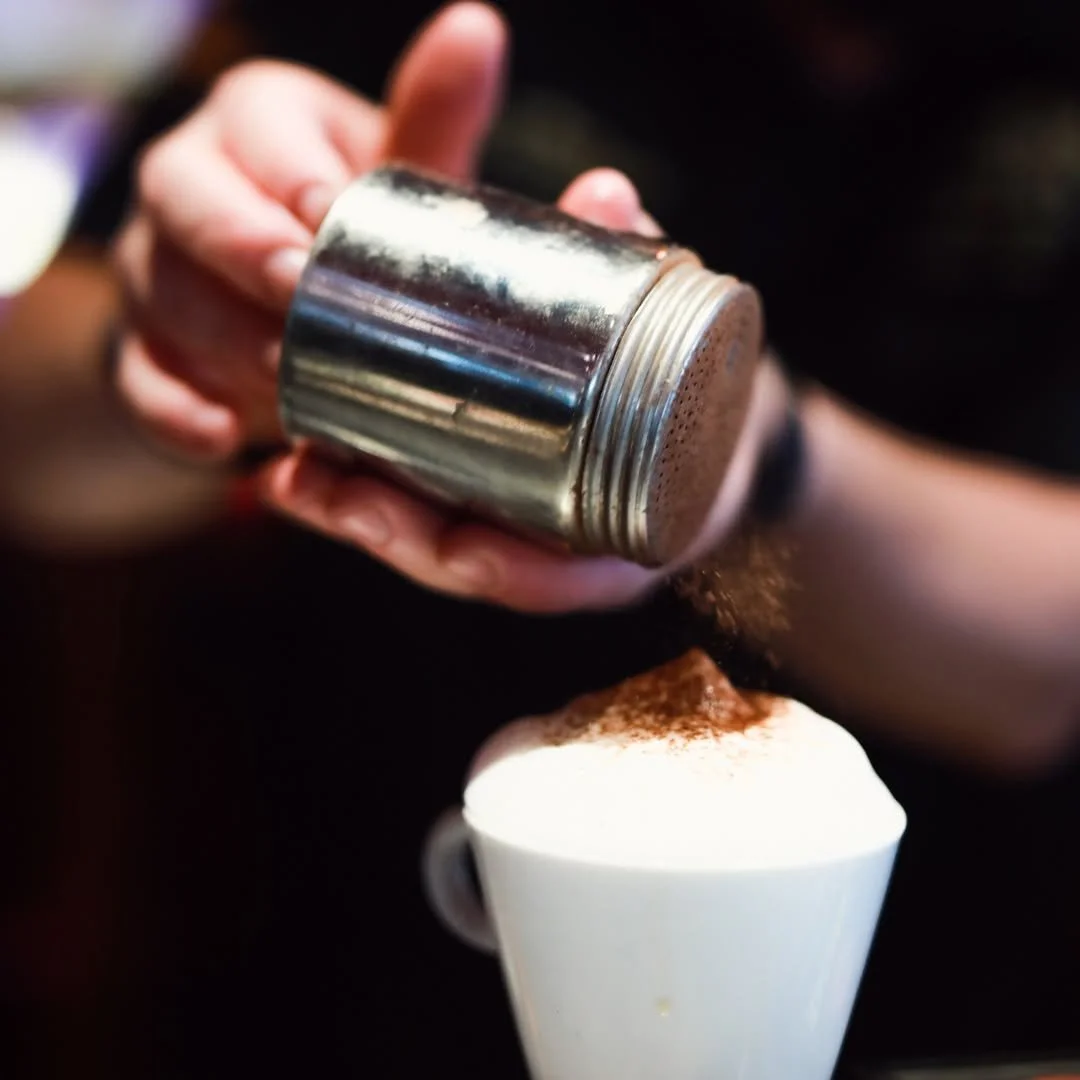 Une main saupoudre du cacao en poudre sur une tasse de café ou de cappuccino.