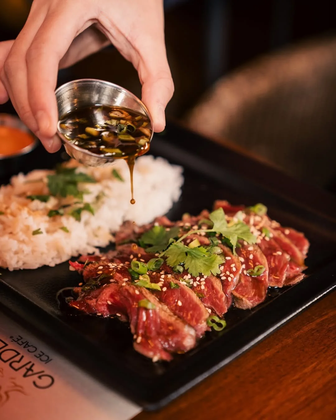 Plat de viande crue assaisonnée avec des légumes verts et du sésame, avec du riz en arrière-plan au Garden Ice Café