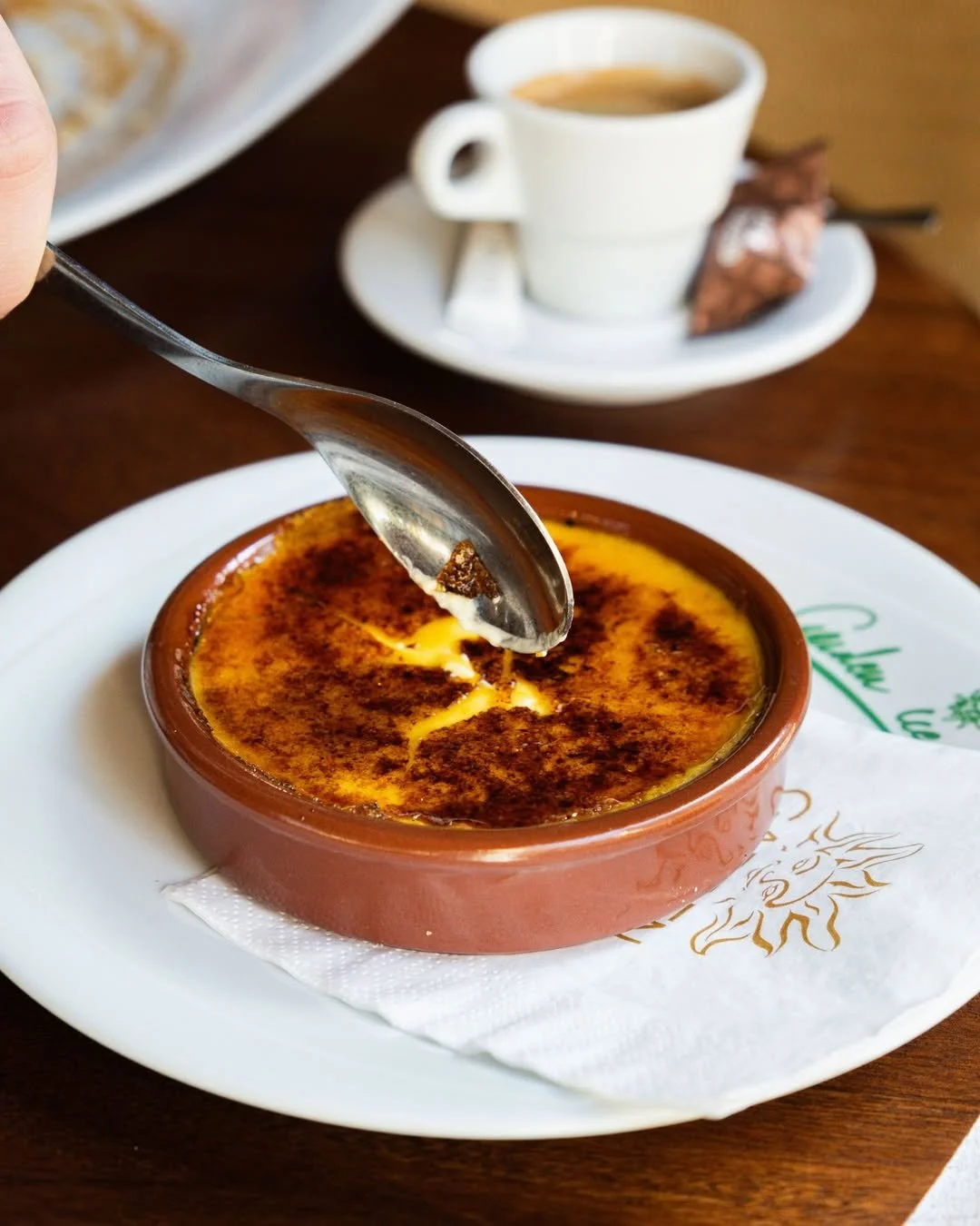 Crème brûlée dans un ramequin en terre cuite, avec une cuillère à soupe en train de casser la croûte caramelisée au Garden Ice Café