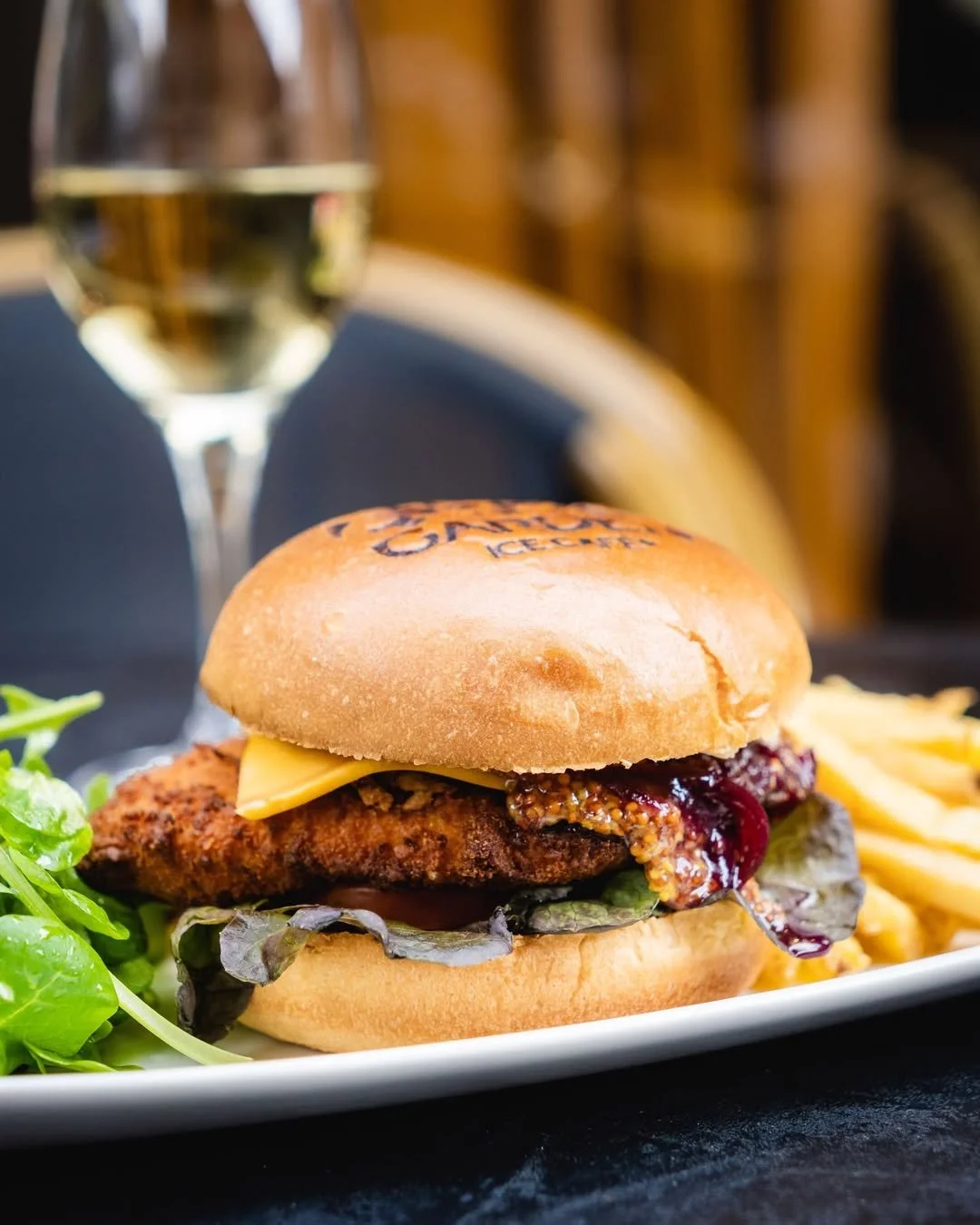 Un sandwich au poulet frit avec du fromage et de la confiture, accompagné de pommes de terre frites et une salade, au Garden Ice Café