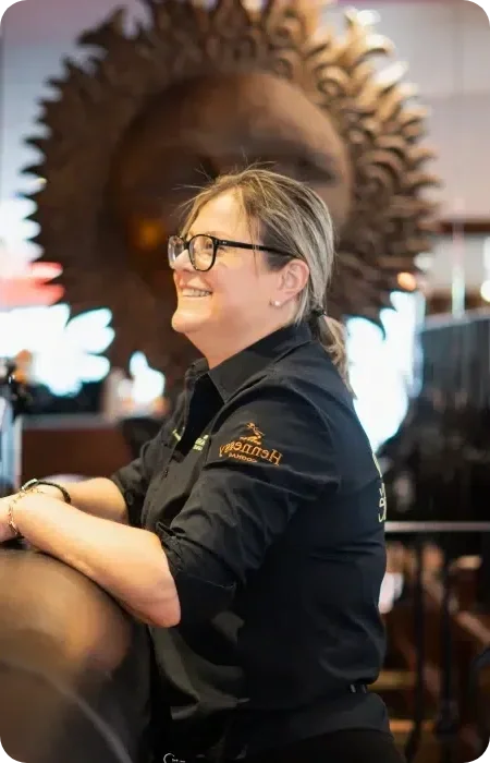 Une femme souriante, portant des lunettes et un uniforme noir, au Garden Ice Café
