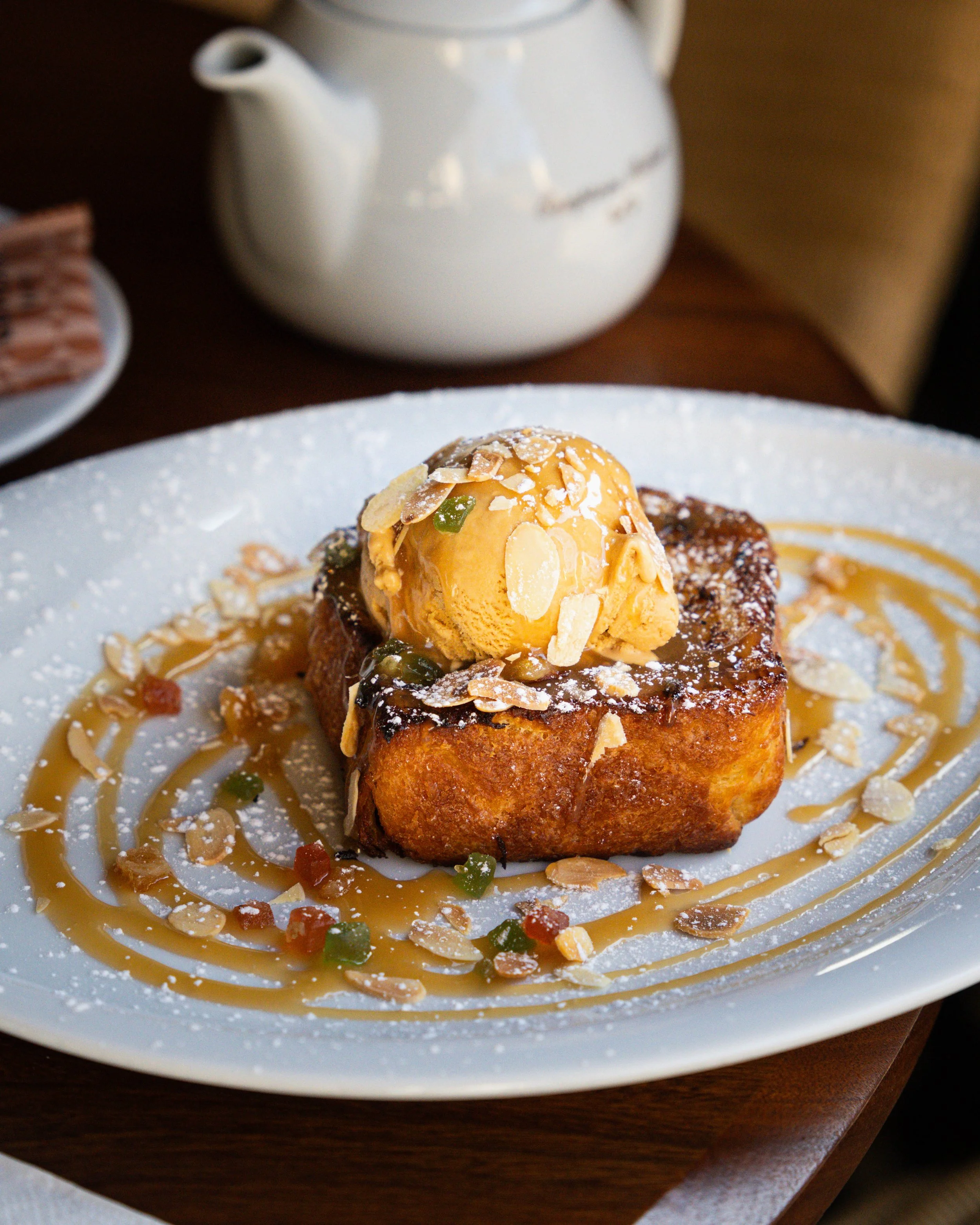 Dessert avec une tranche de pain perdu garnie de glace à la vanille, amandes effilées, sauce caramel, et petits morceaux de fruits confits, présenté sur une assiette blanche
