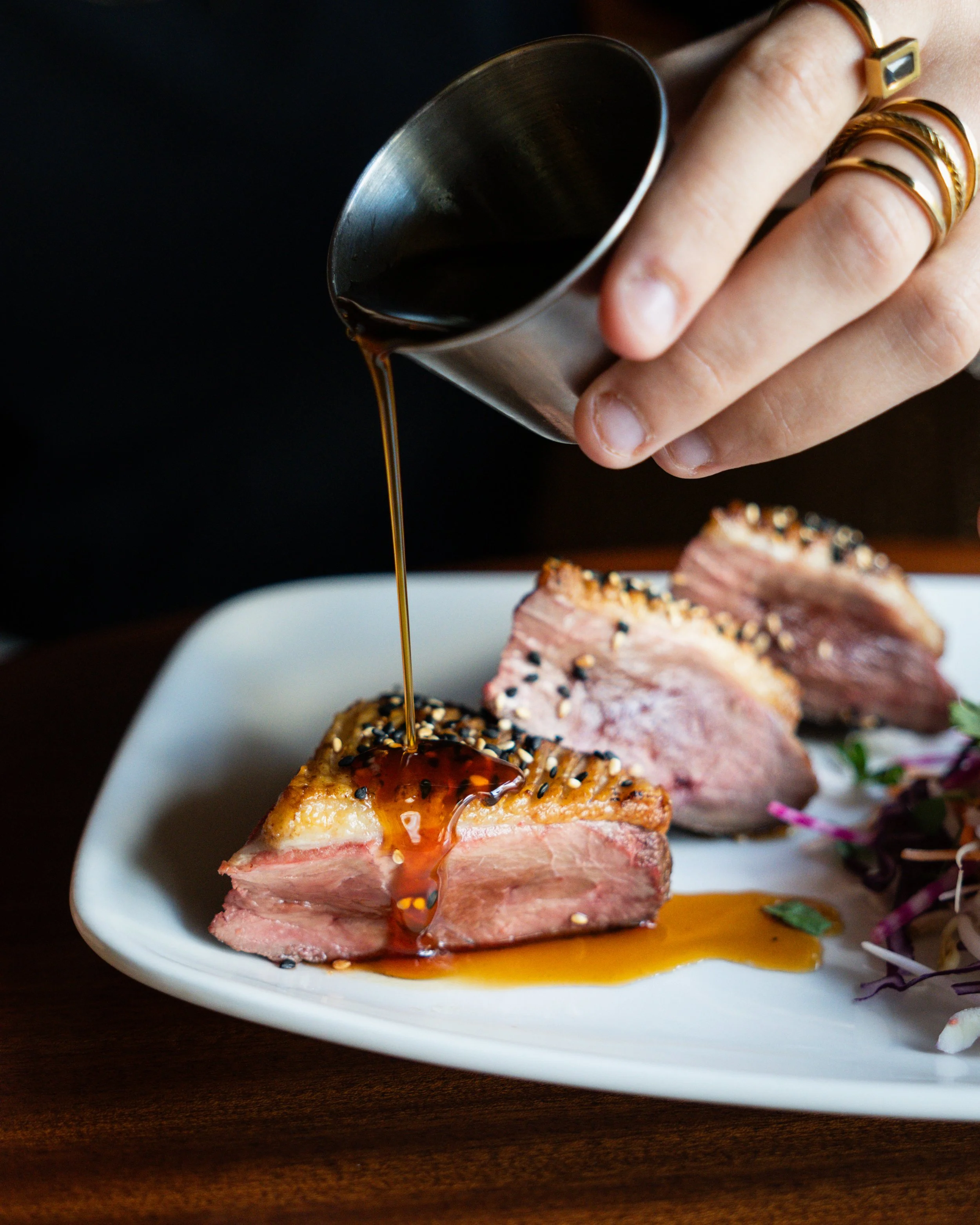 Une main verse une sauce sur des tranches de viande crue, présentées avec du riz et des légumes, au Garden Ice Café