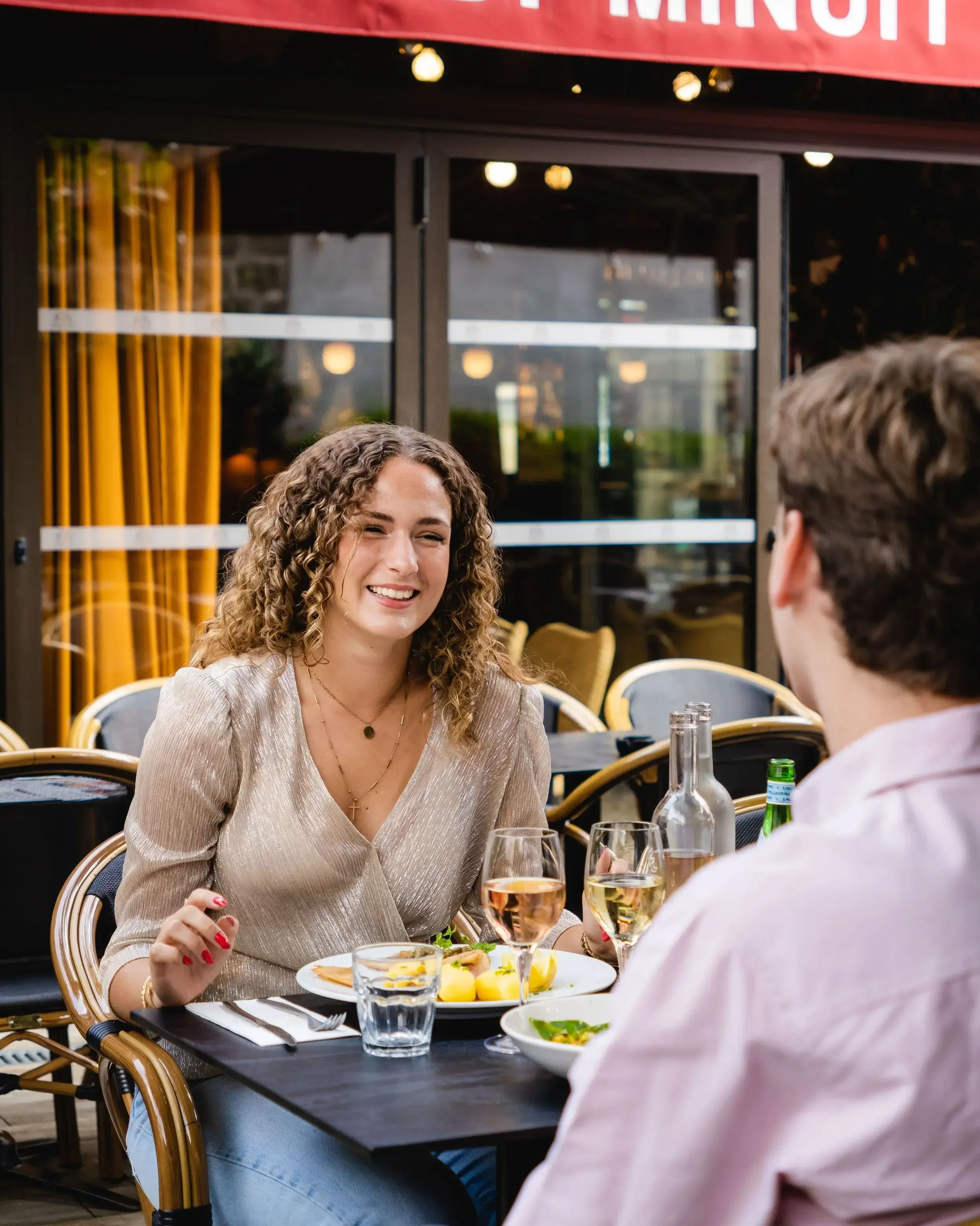 Une femme souriante en train de dîner avec un homme au Garden Ice Café, avec des plats, des bouteilles et des verres sur la table.