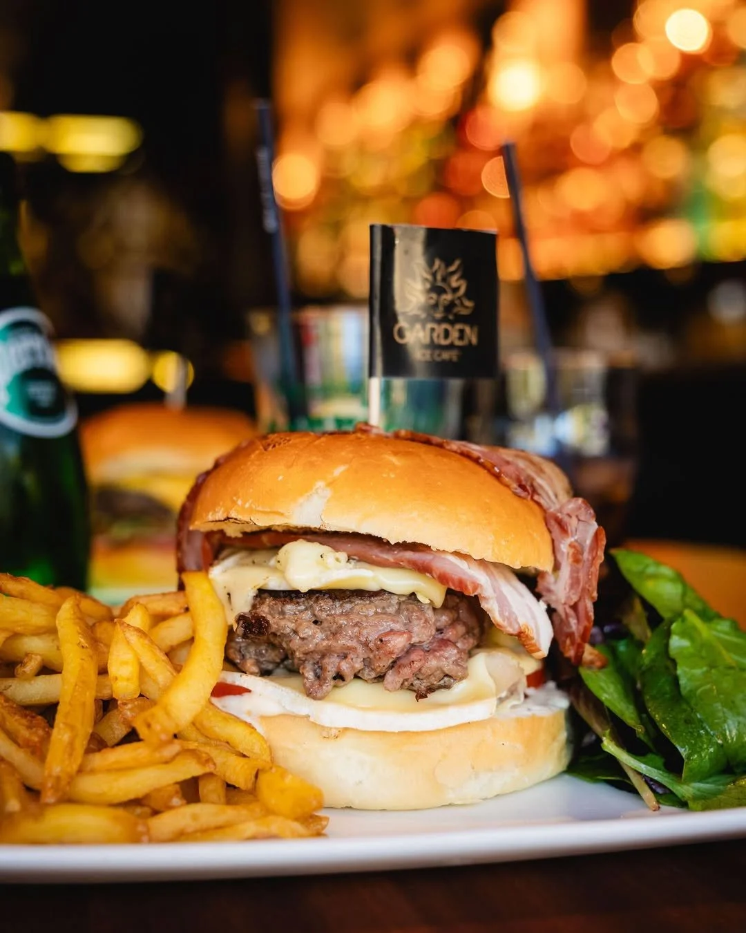 Un hamburger avec du fromage, du steak, du bacon, des frites et une salade verte, servi au Garden Ice Café