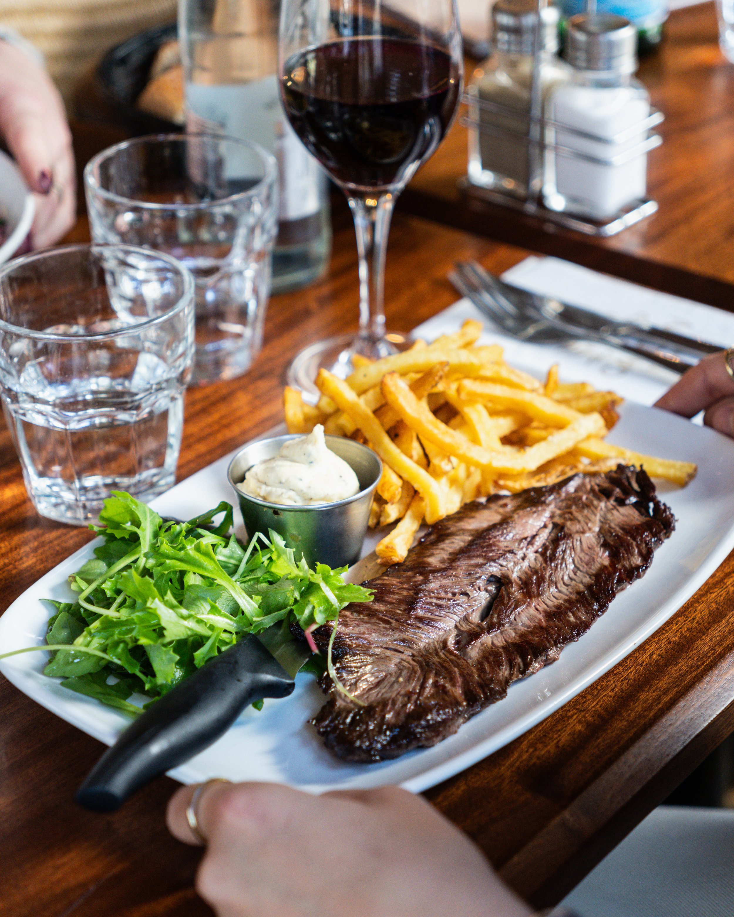 Assiette avec une côte de bœuf, des frites, une salade verte, une sauce, un verre de vin rouge, deux verres d'eau et des condiments au Garden Ice Café