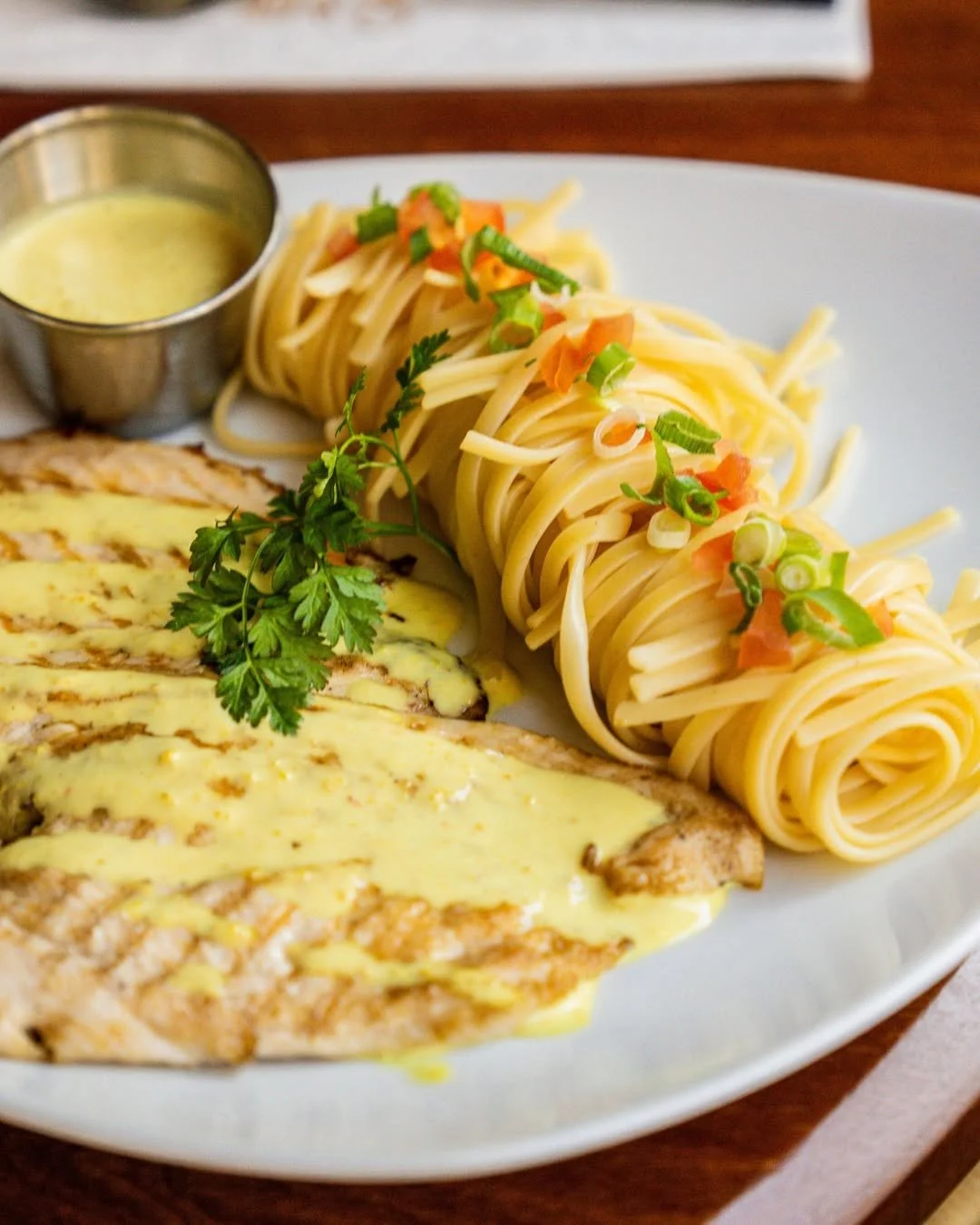 Assiette de pâtes aux légumes garnie de ciboulette, accompagnée d'une tranche de poulet avec une sauce jaune et un petit bol de sauce à côté au Garden Ice Café