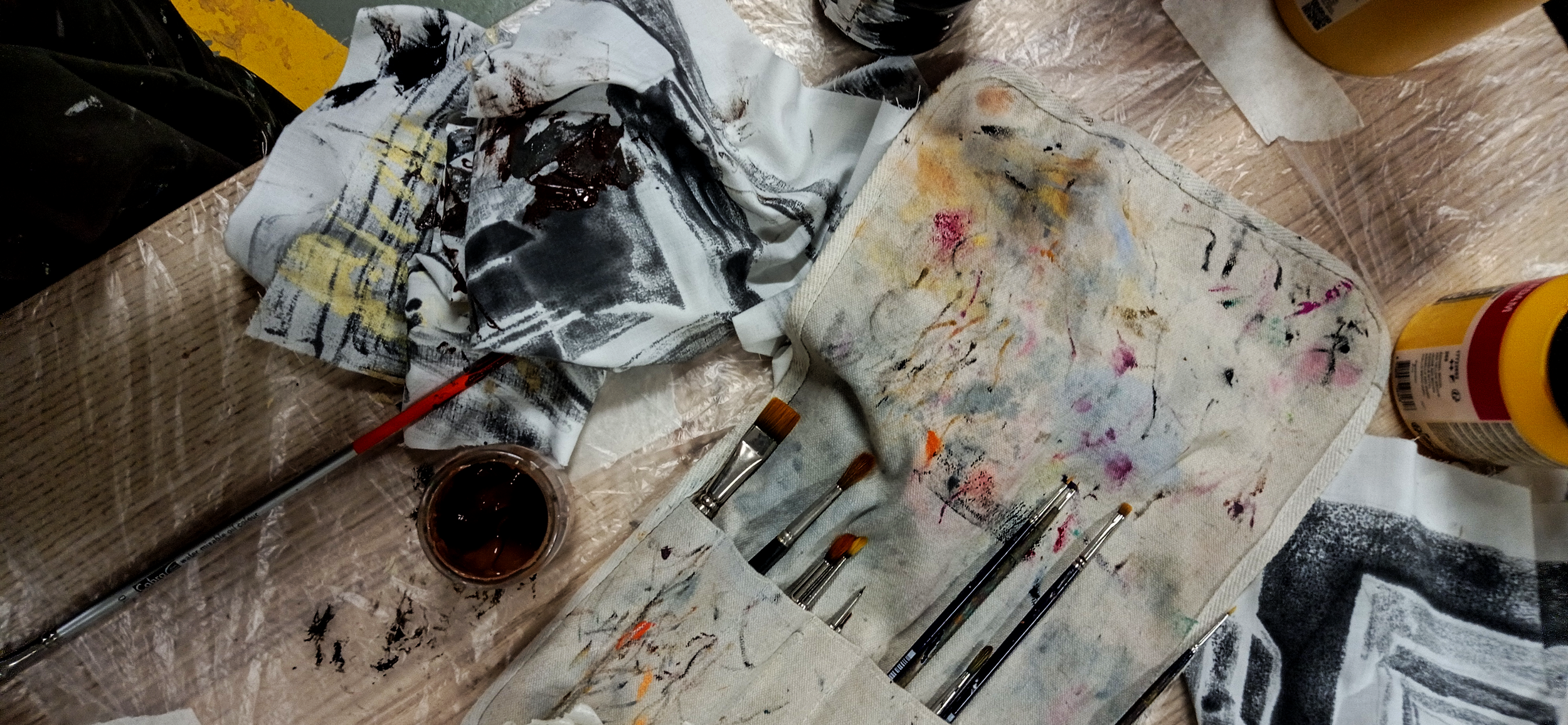 Mesa de trabalho de um artista com tinta, pincéis e panos sujos de tinta.