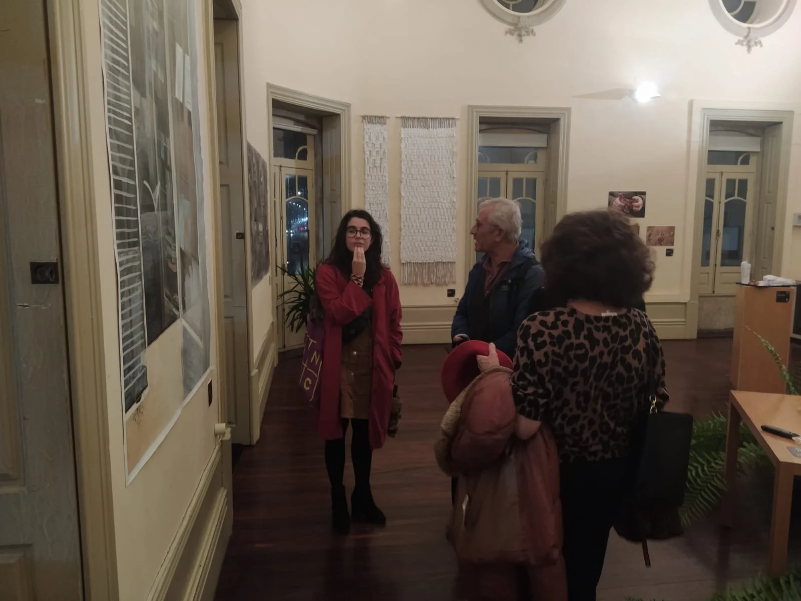 Quatro pessoas conversando em uma sala de exposições com paredes decoradas e janelas.