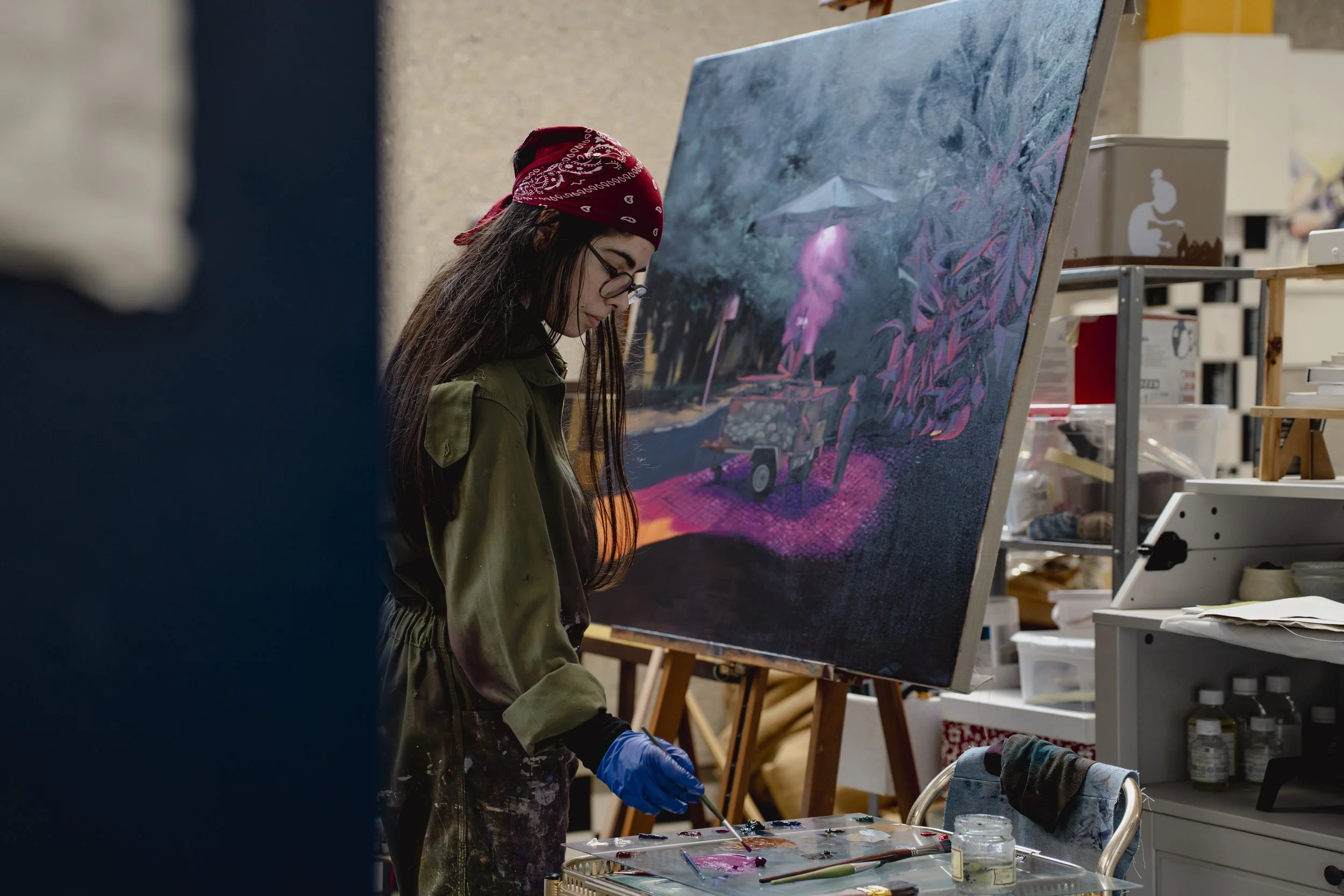 Jovem artista pintando uma tela com cenas de uma floresta e uma máquina, em um estúdio de arte.