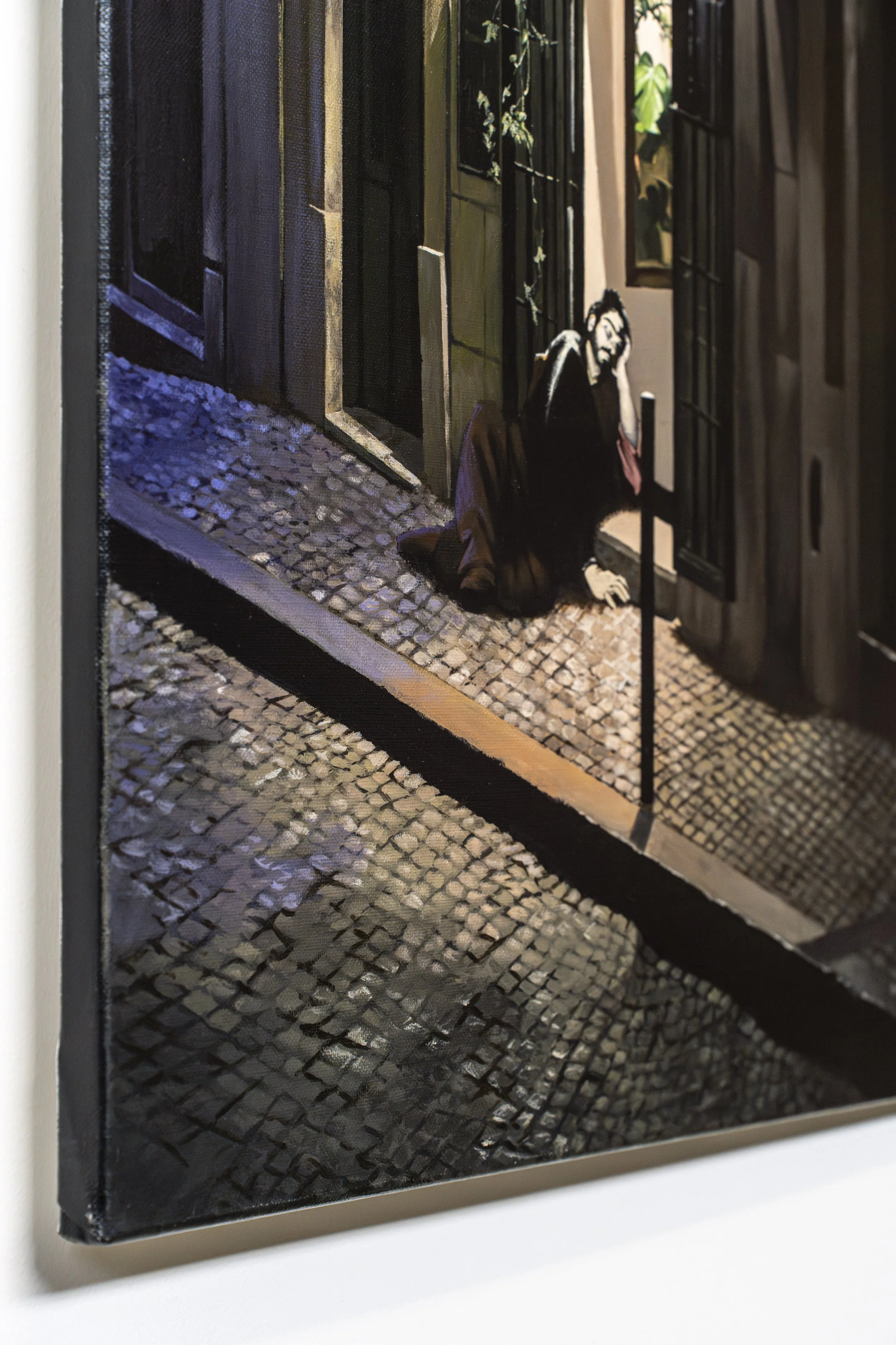 Pessoa sentada no chão com uma mão na cabeça, ao lado de uma porta de vidro em uma rua de paralelepípedos à noite.